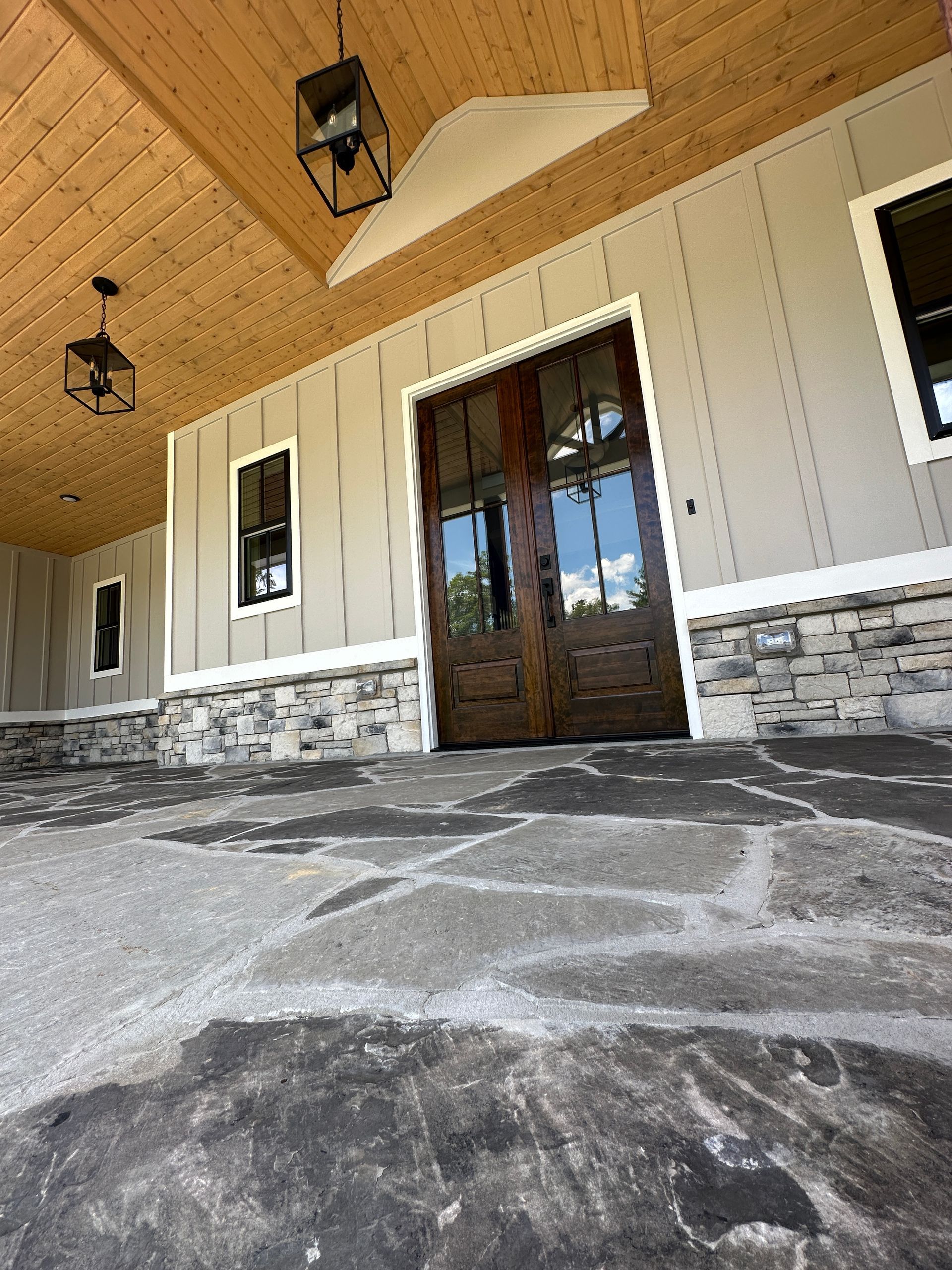 Covered front porch with stone flooring, white siding, wood ceiling, and double glass entry doors