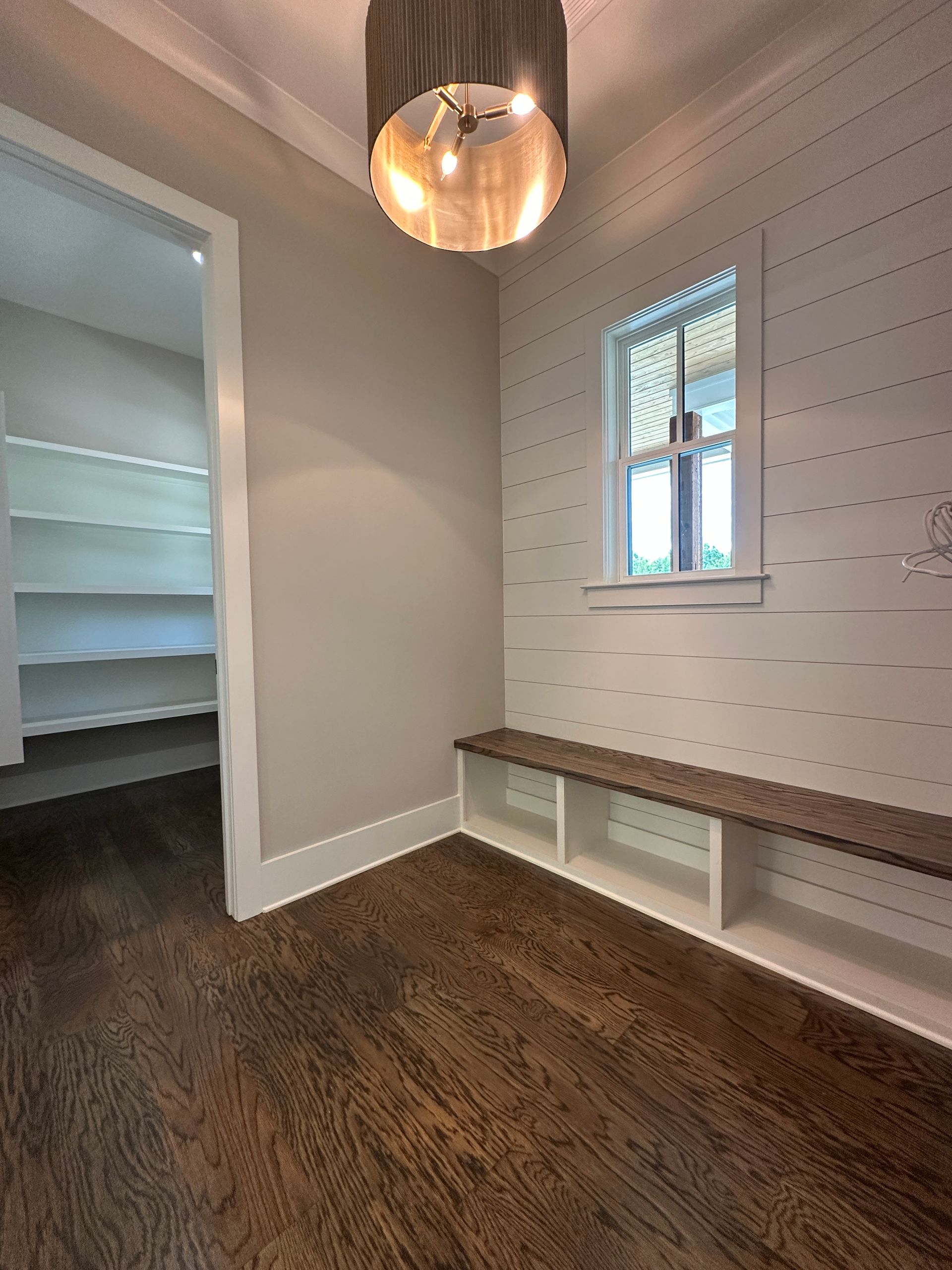 Empty entryway with dark wood floor, white walls, built-in bench, pendant light, and doorway to a closet.