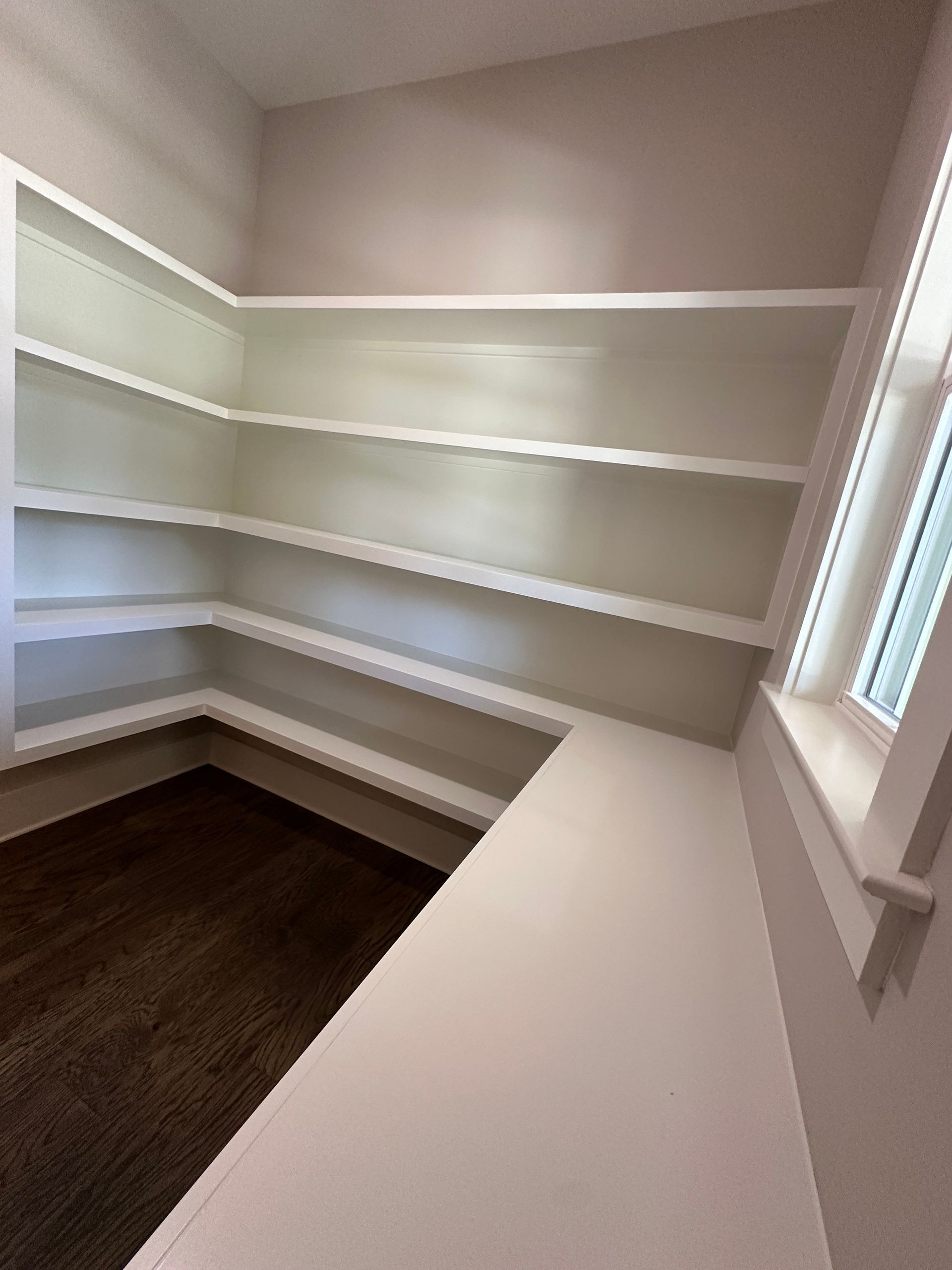 Empty walk-in closet with white shelves, beige walls, and a dark wood floor.