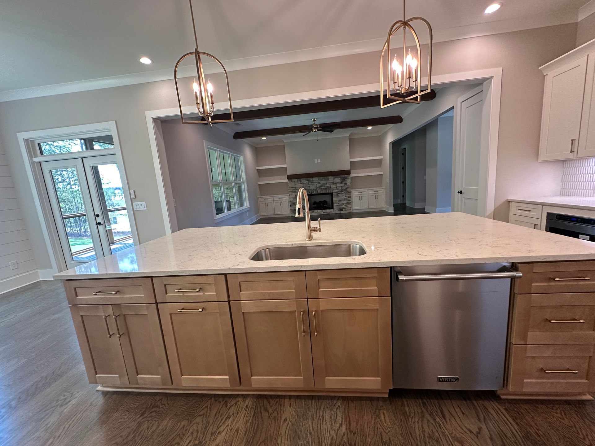 Modern kitchen with a large island, white countertops, wood cabinets, pendant lights, and stainless dishwasher
