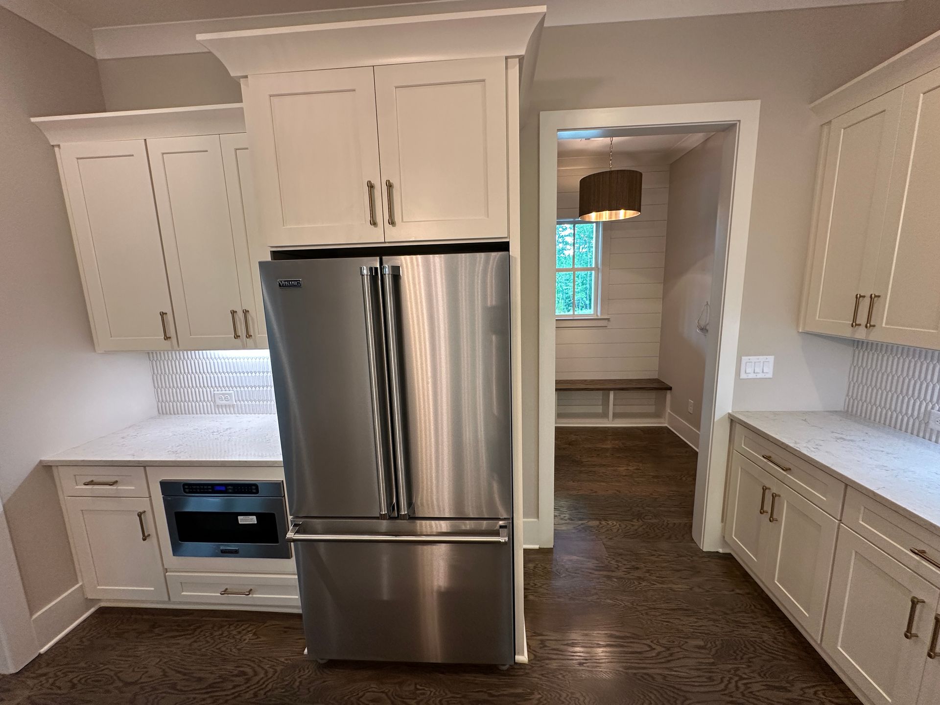 Bright kitchen with white cabinets, stainless steel fridge, and doorway to a dining room.