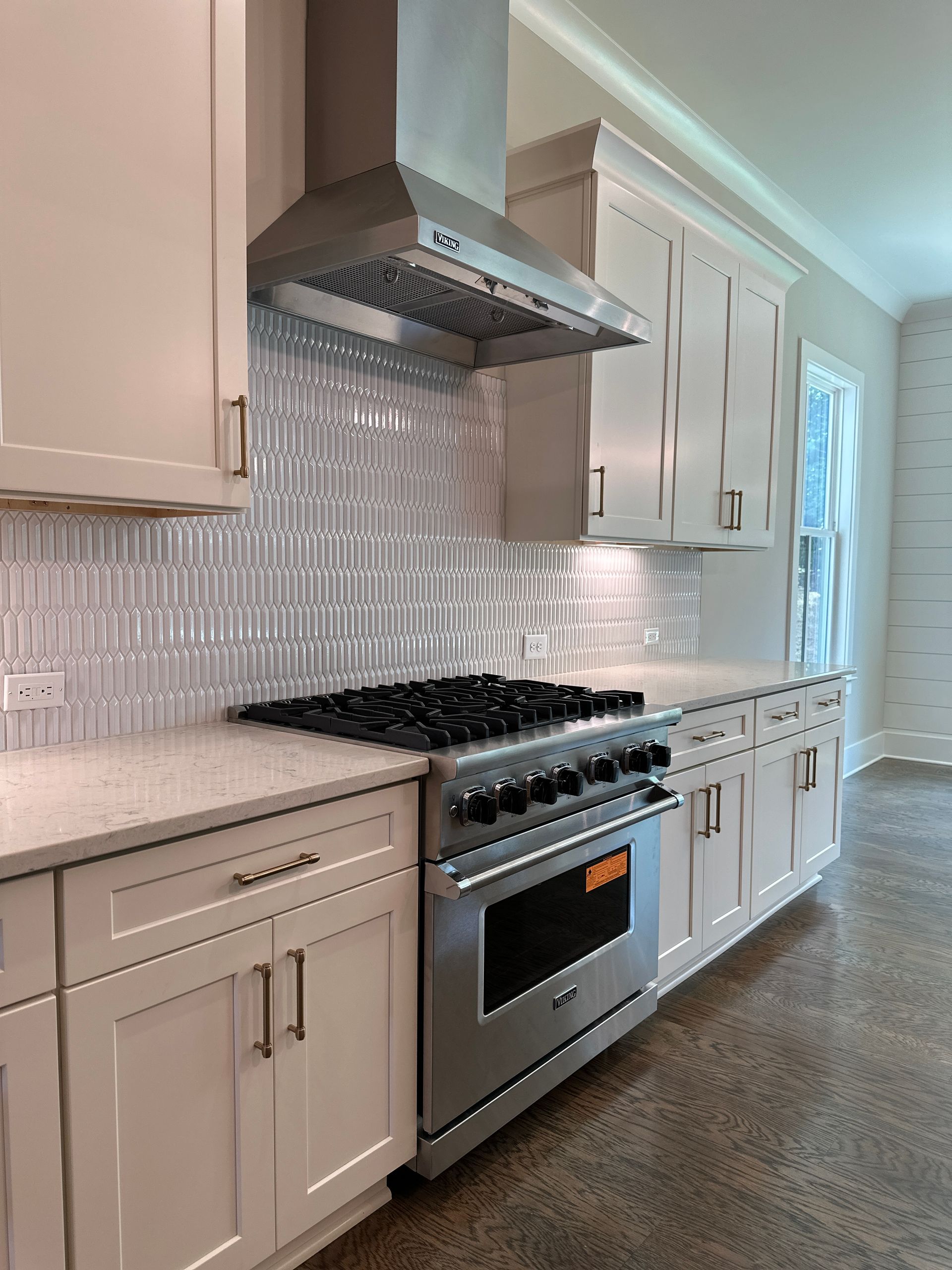 Bright modern kitchen with cream cabinets, stainless steel range, and white mosaic tile backsplash.