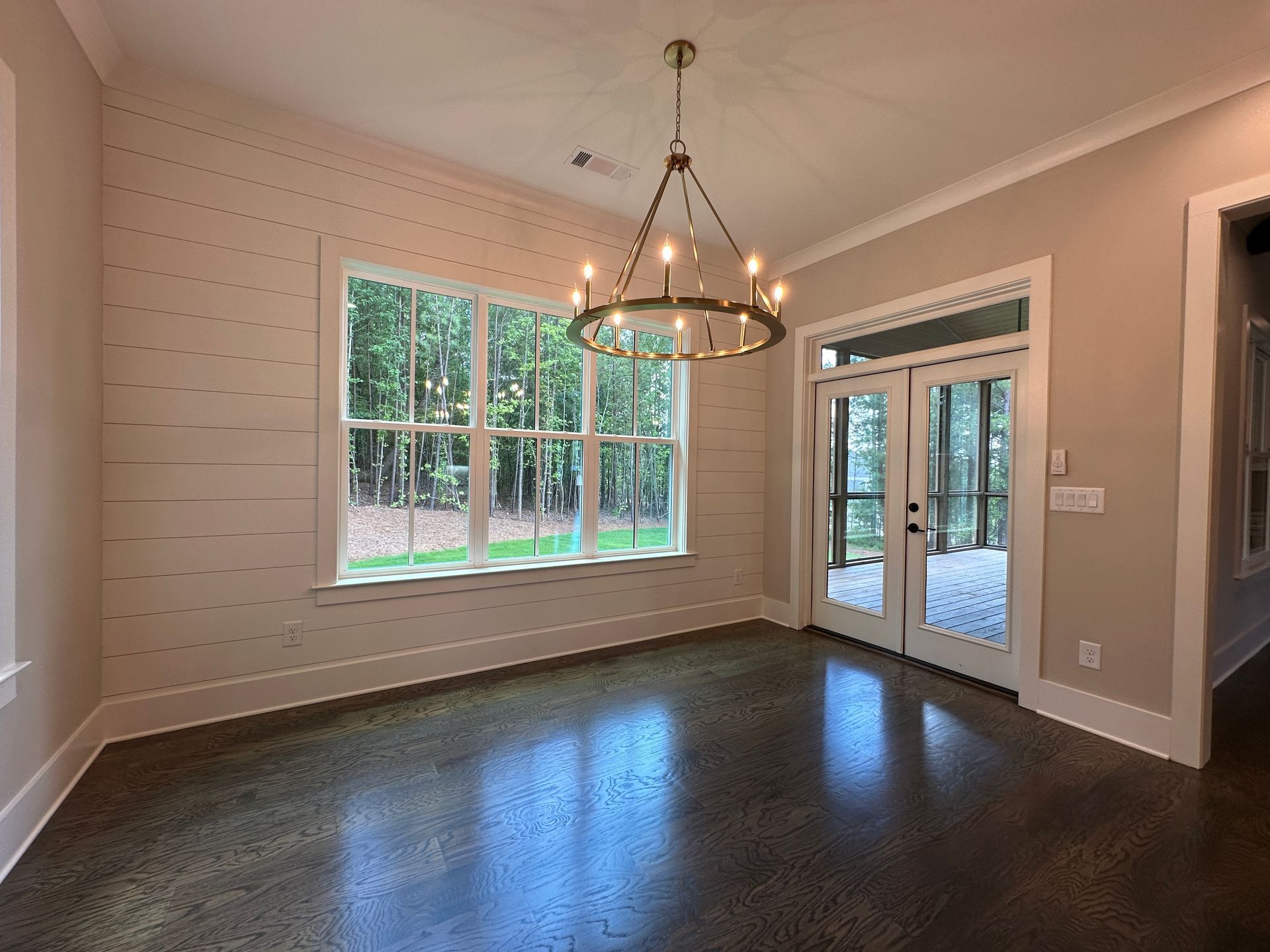 Empty dining room with dark wood floor, chandelier, large window, and glass French doors to a patio.