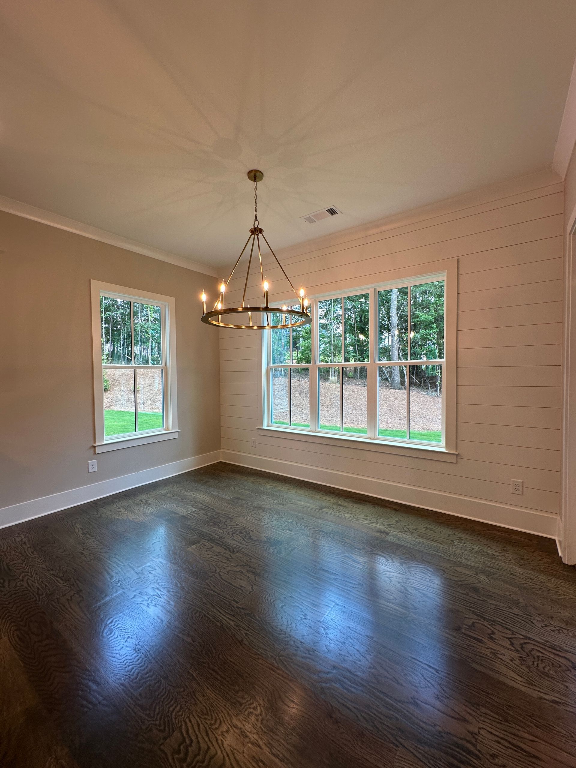 Empty dining room with dark hardwood floors, chandelier, and large windows letting in daylight