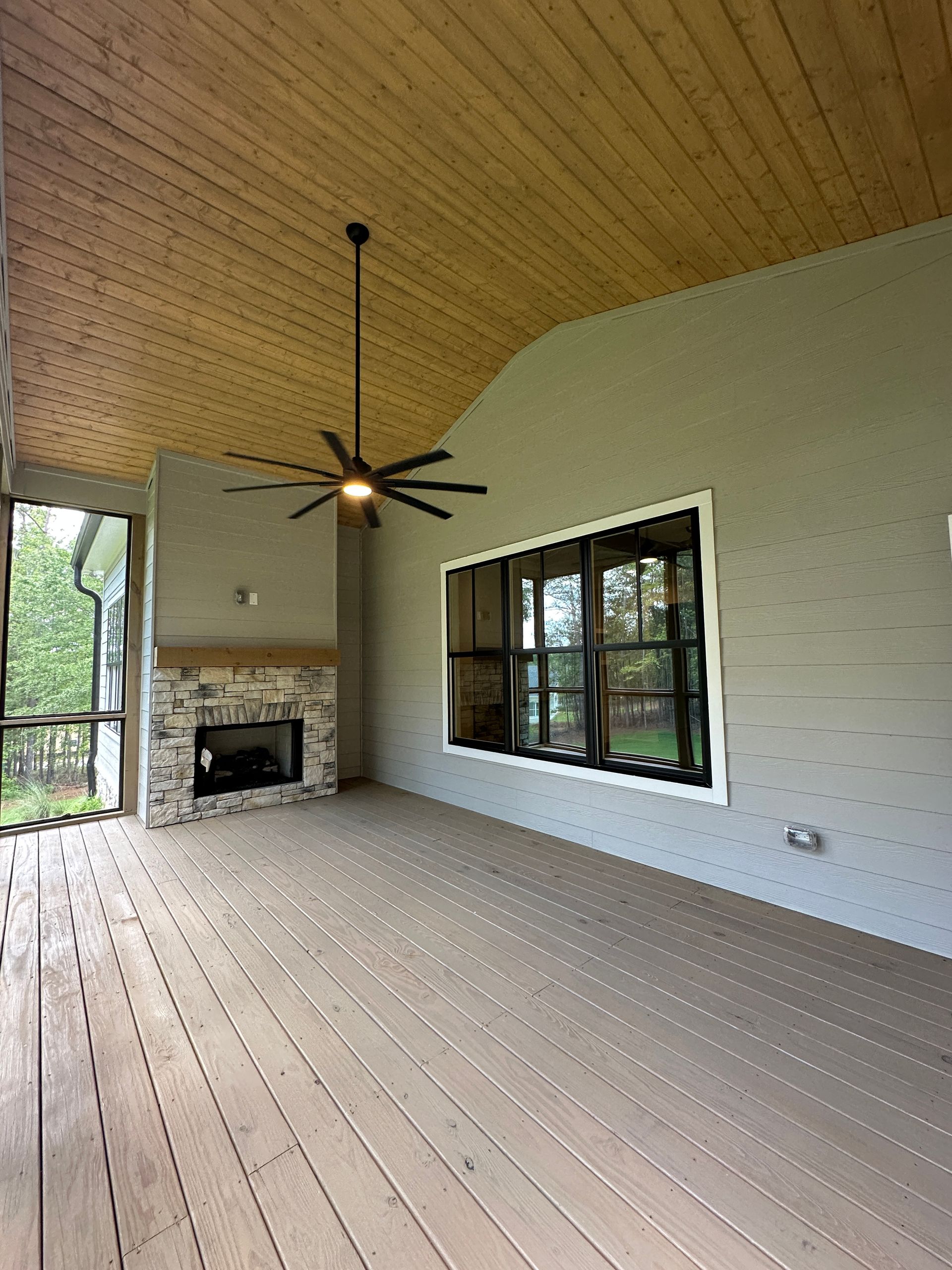 Covered patio with wood ceiling, ceiling fan, fireplace, and large windows overlooking greenery