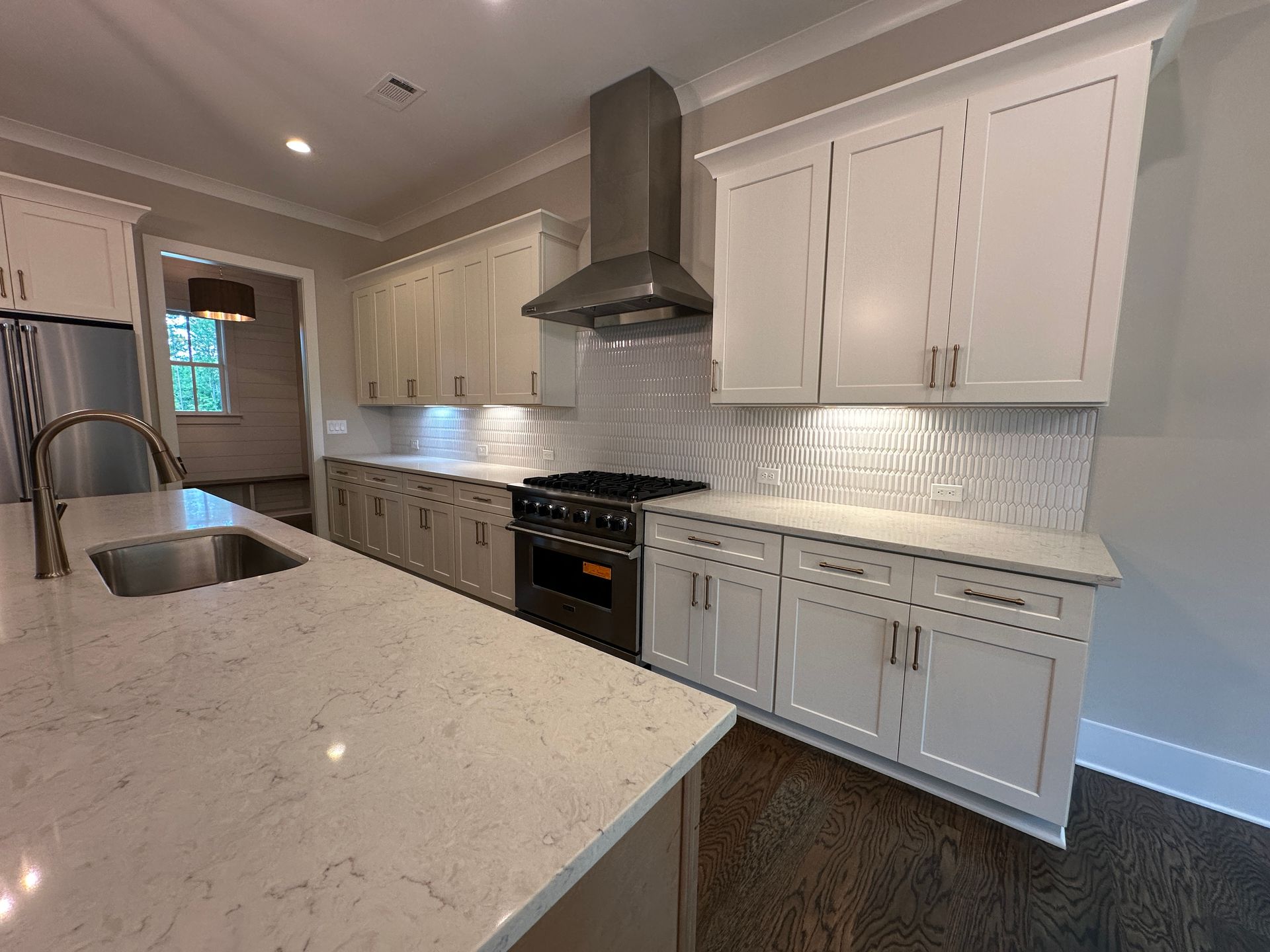 Bright modern kitchen with white cabinets, marble island, stainless appliances, and gray backsplash