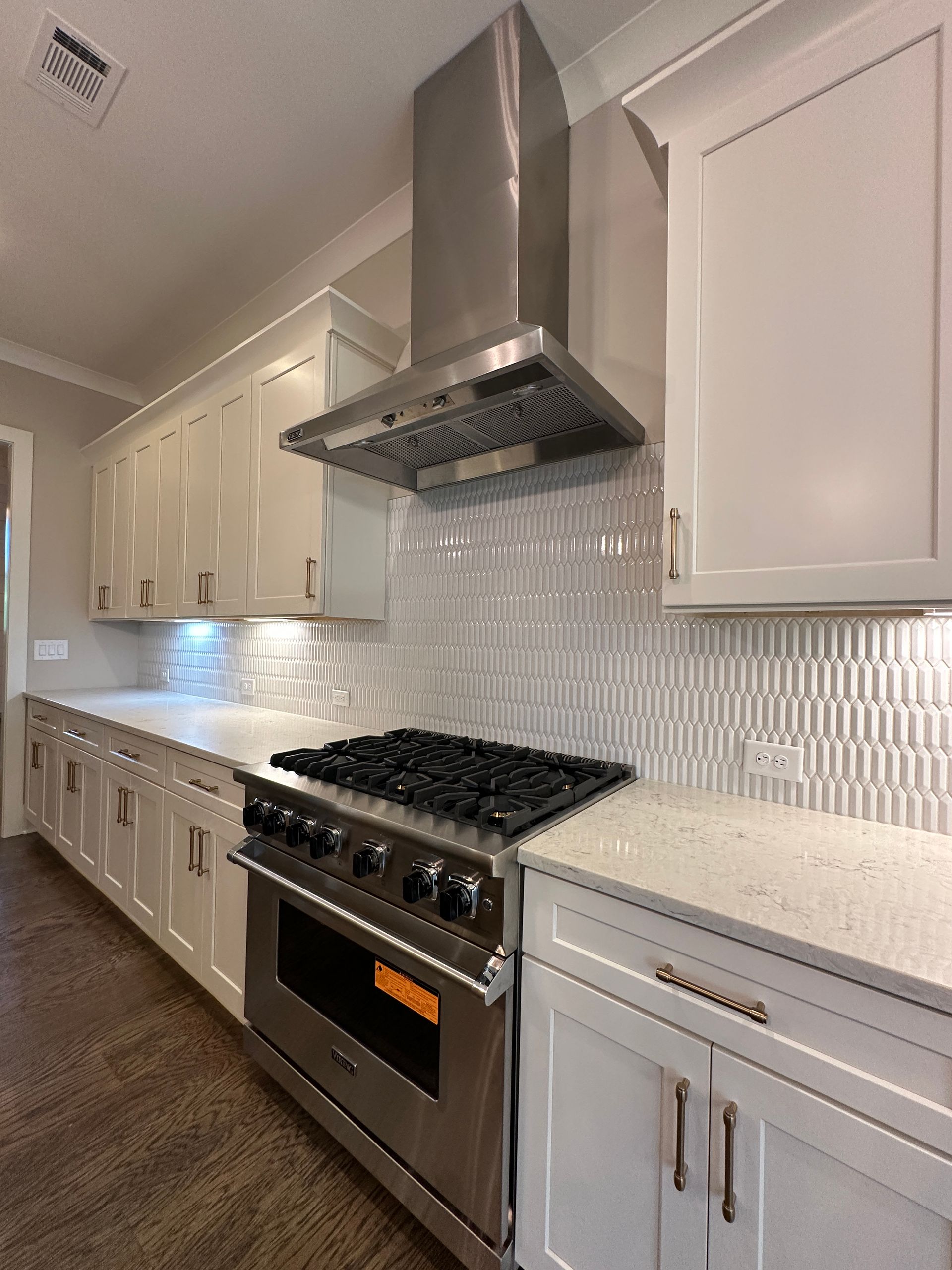 Modern kitchen with stainless steel range hood, gas stove, white cabinets, and herringbone backsplash