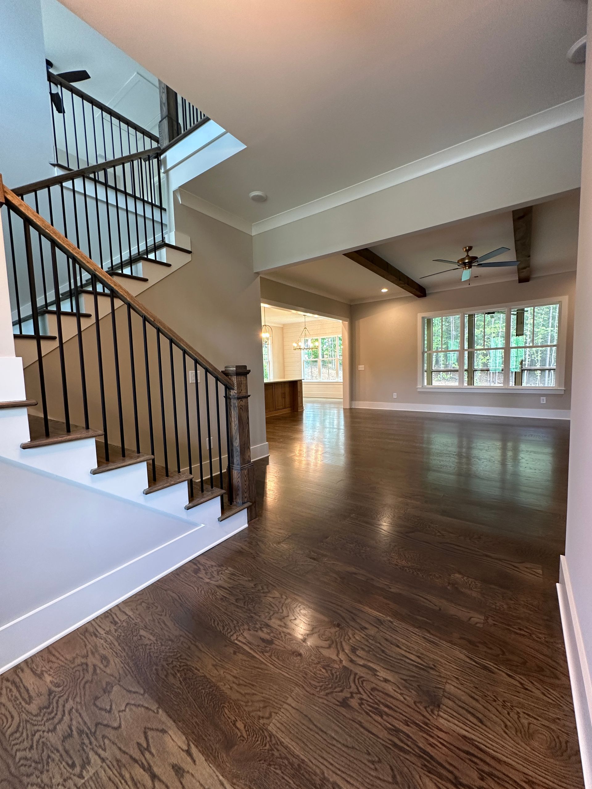 Spacious empty living room with hardwood floors, staircase, and large windows letting in natural light
