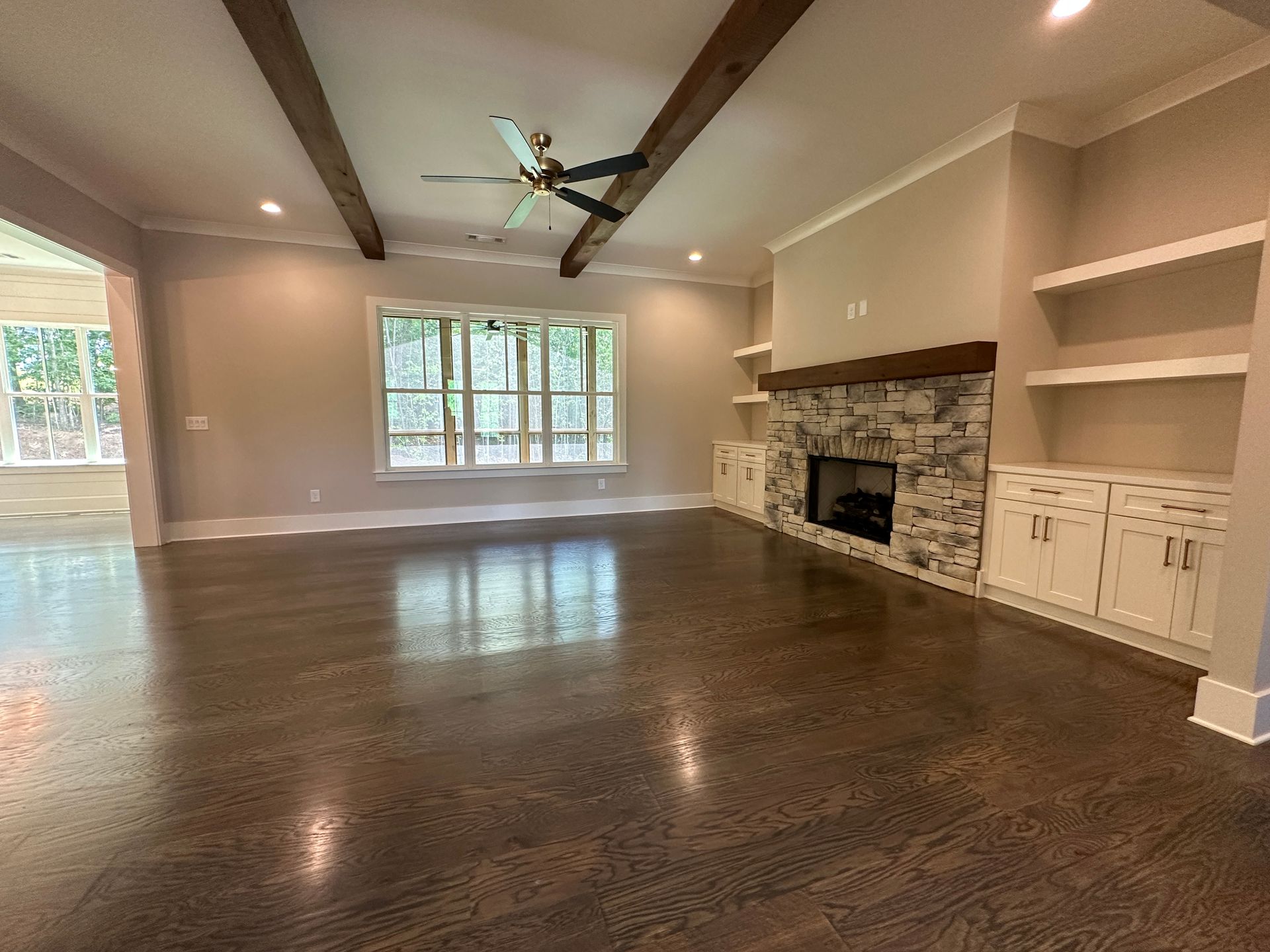 Spacious living room with dark wood floors, exposed beams, fireplace, and built-in shelves.
