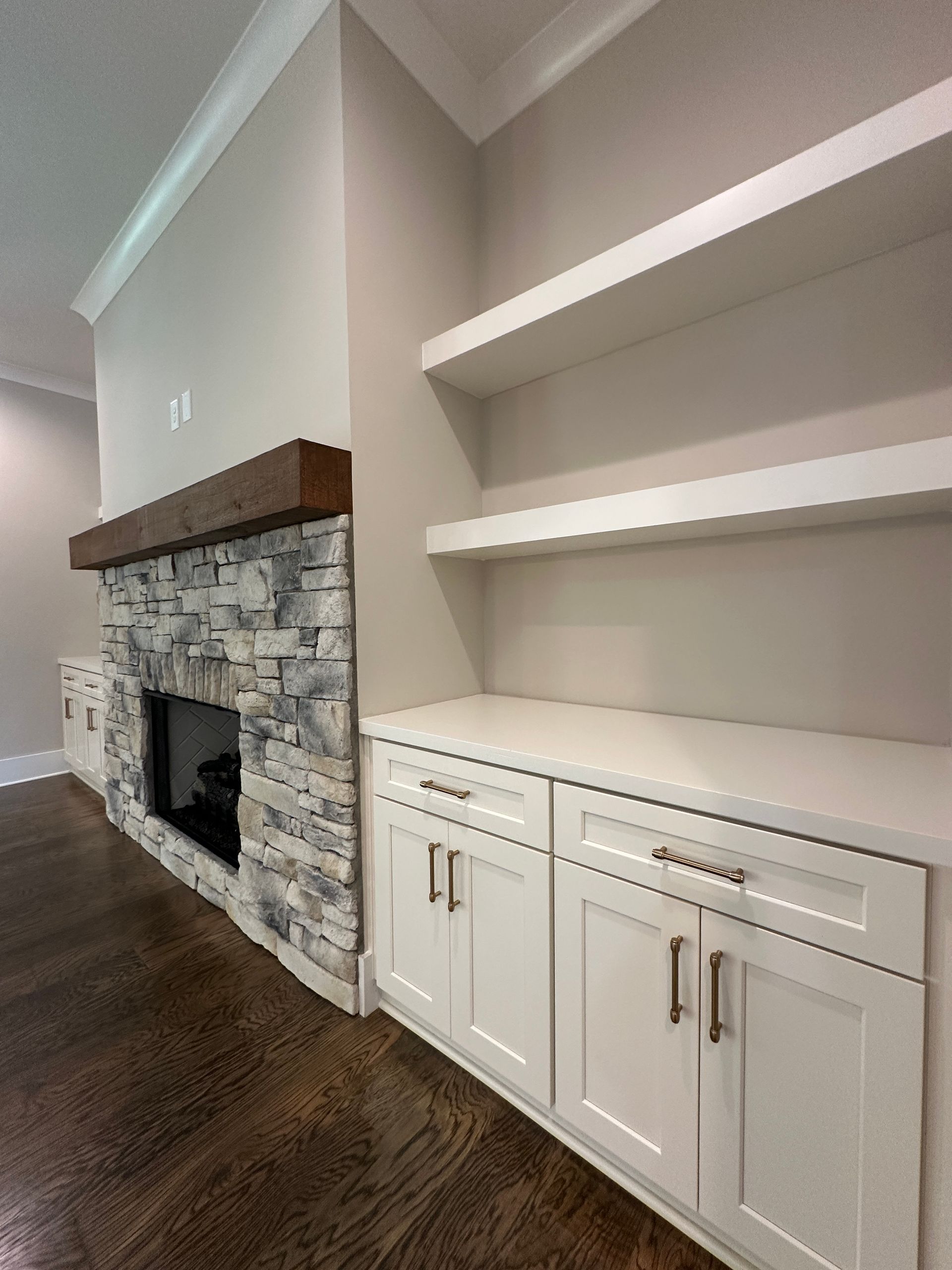 Living room with stone fireplace, white built-in cabinets, and dark hardwood floor