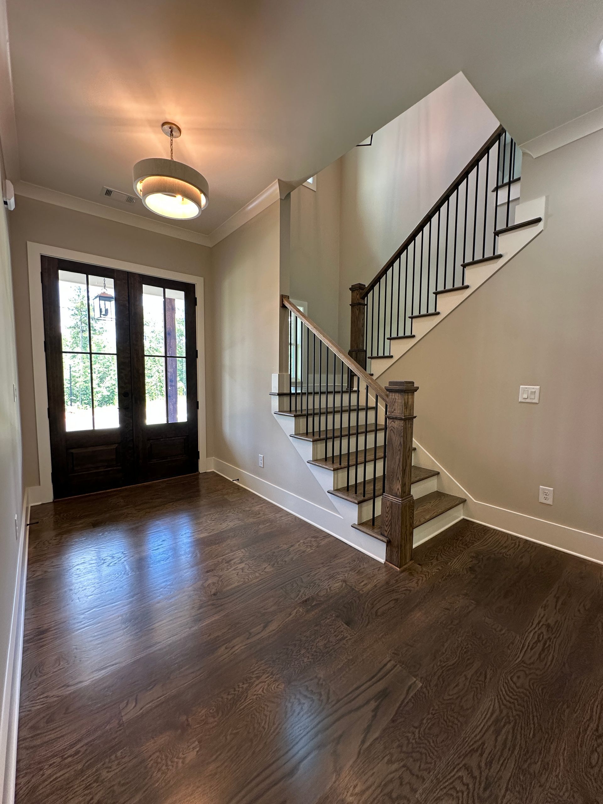 Empty foyer with dark wood floor, staircase, and front door with sidelights.