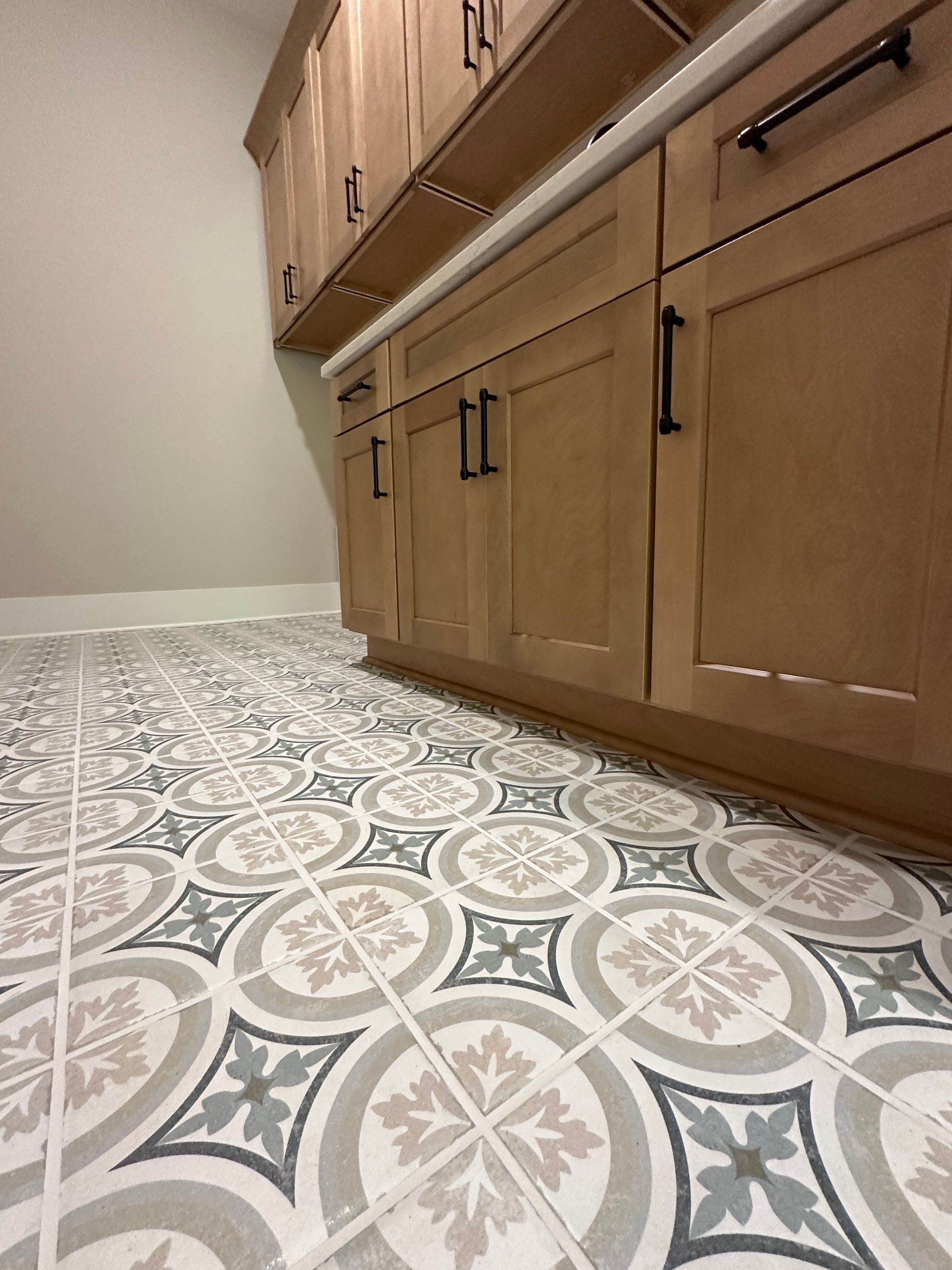 Low-angle view of a kitchen with wood cabinets and patterned tile flooring.