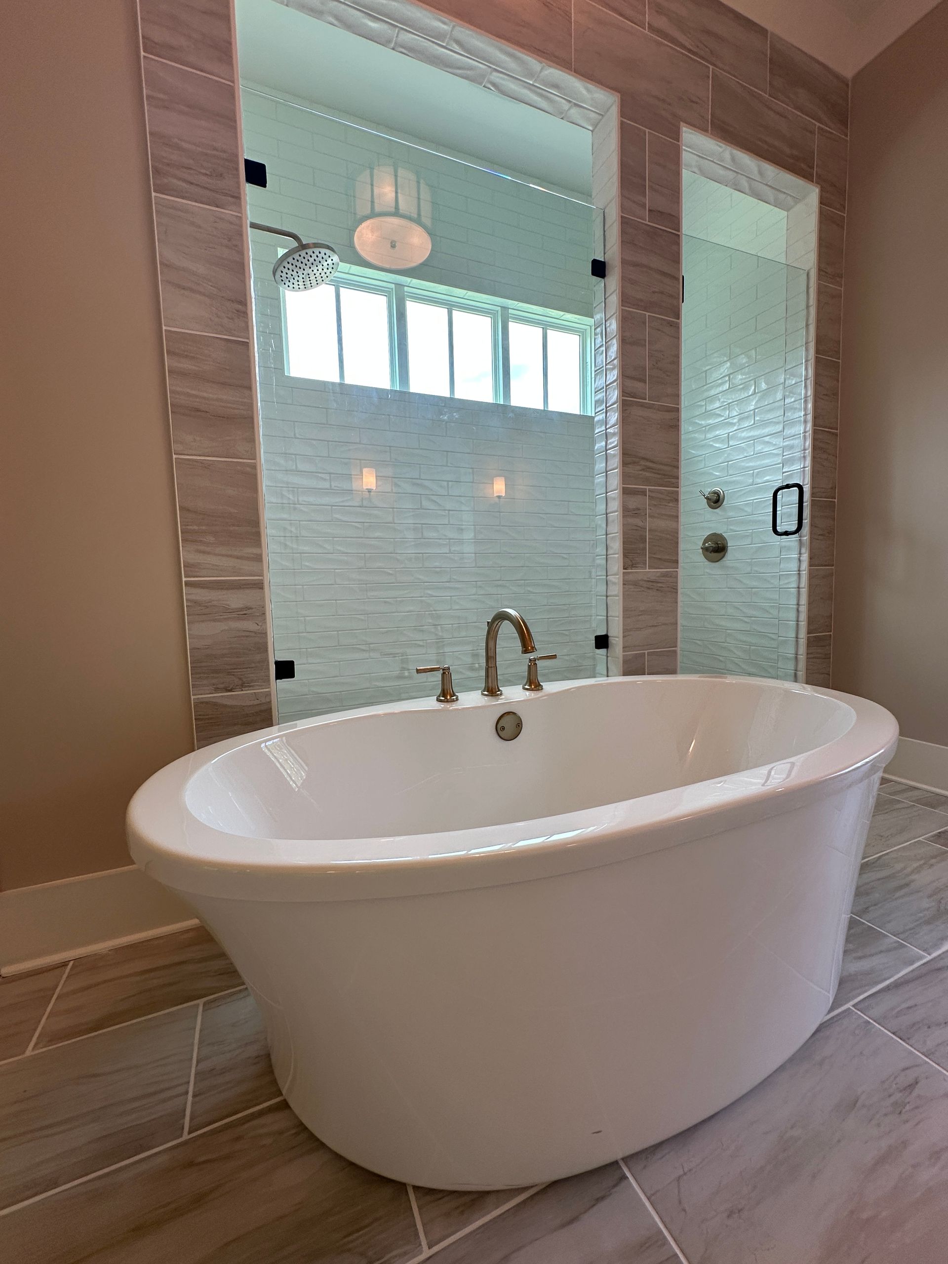 Freestanding white bathtub in a modern bathroom with glass shower walls and wood-look tile flooring