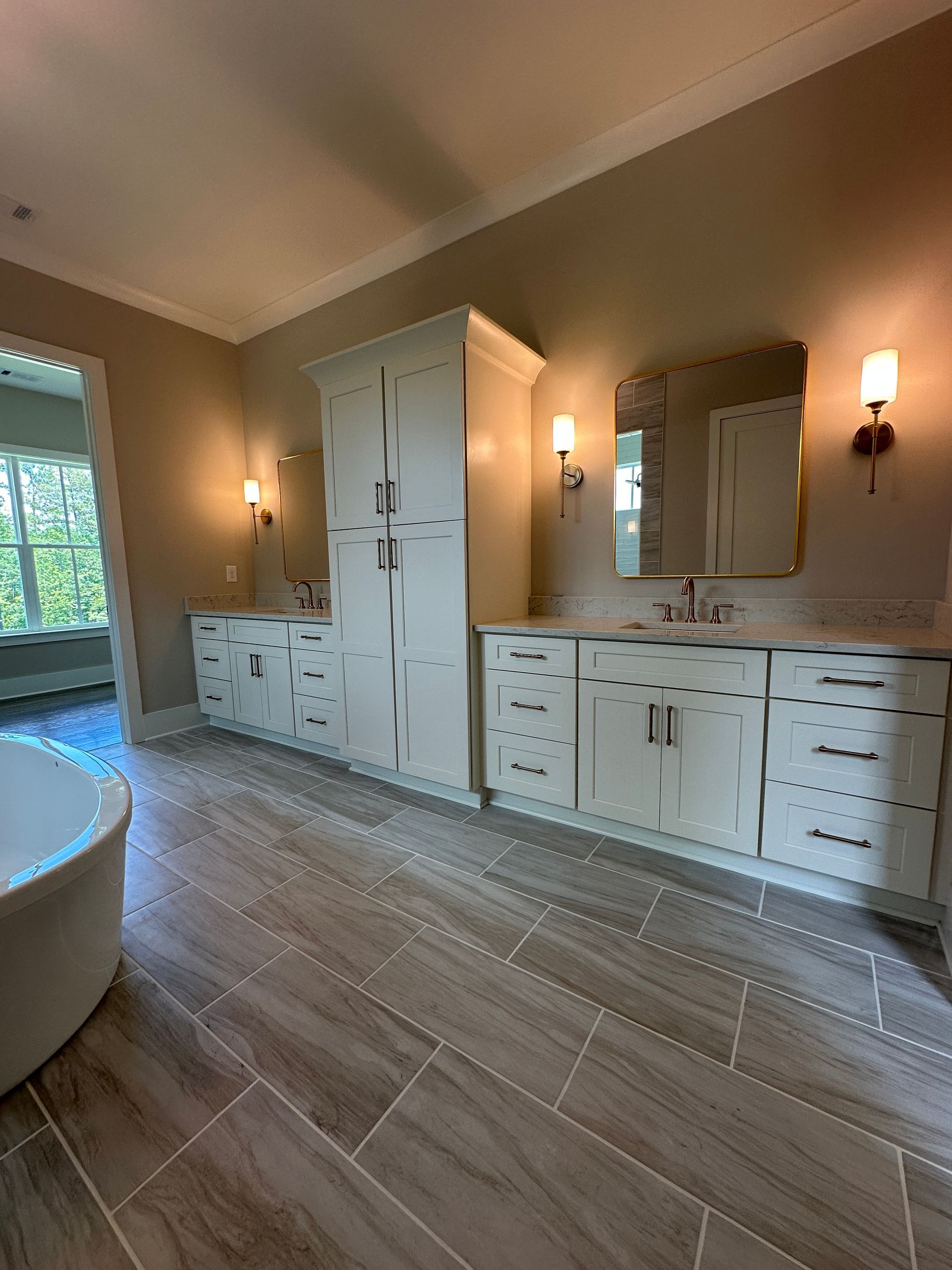 Modern bathroom with white cabinets, double vanity, mirror, sconces, and large wood-look tile floor.