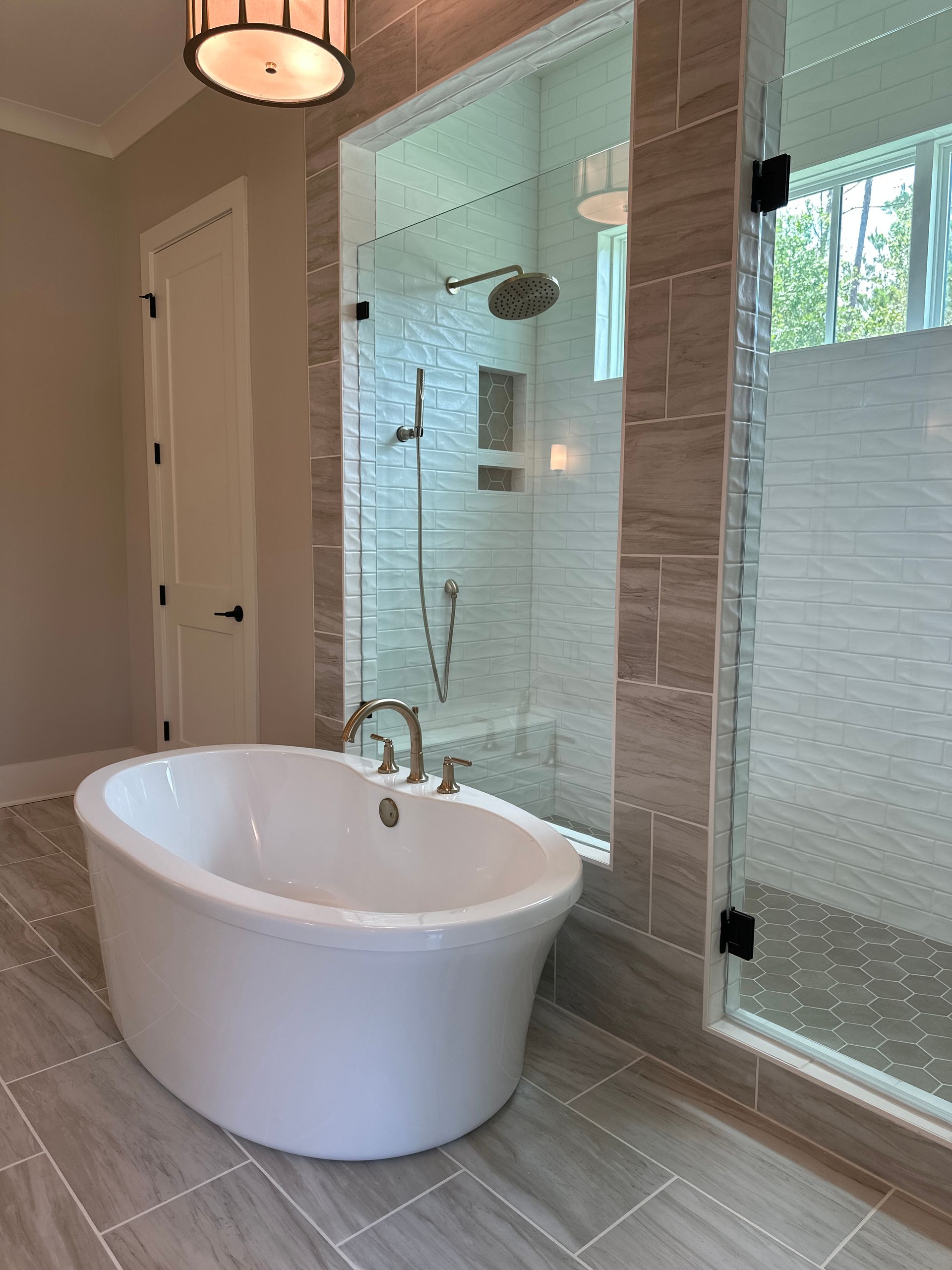 Modern bathroom with freestanding white tub, glass shower, and frosted window.