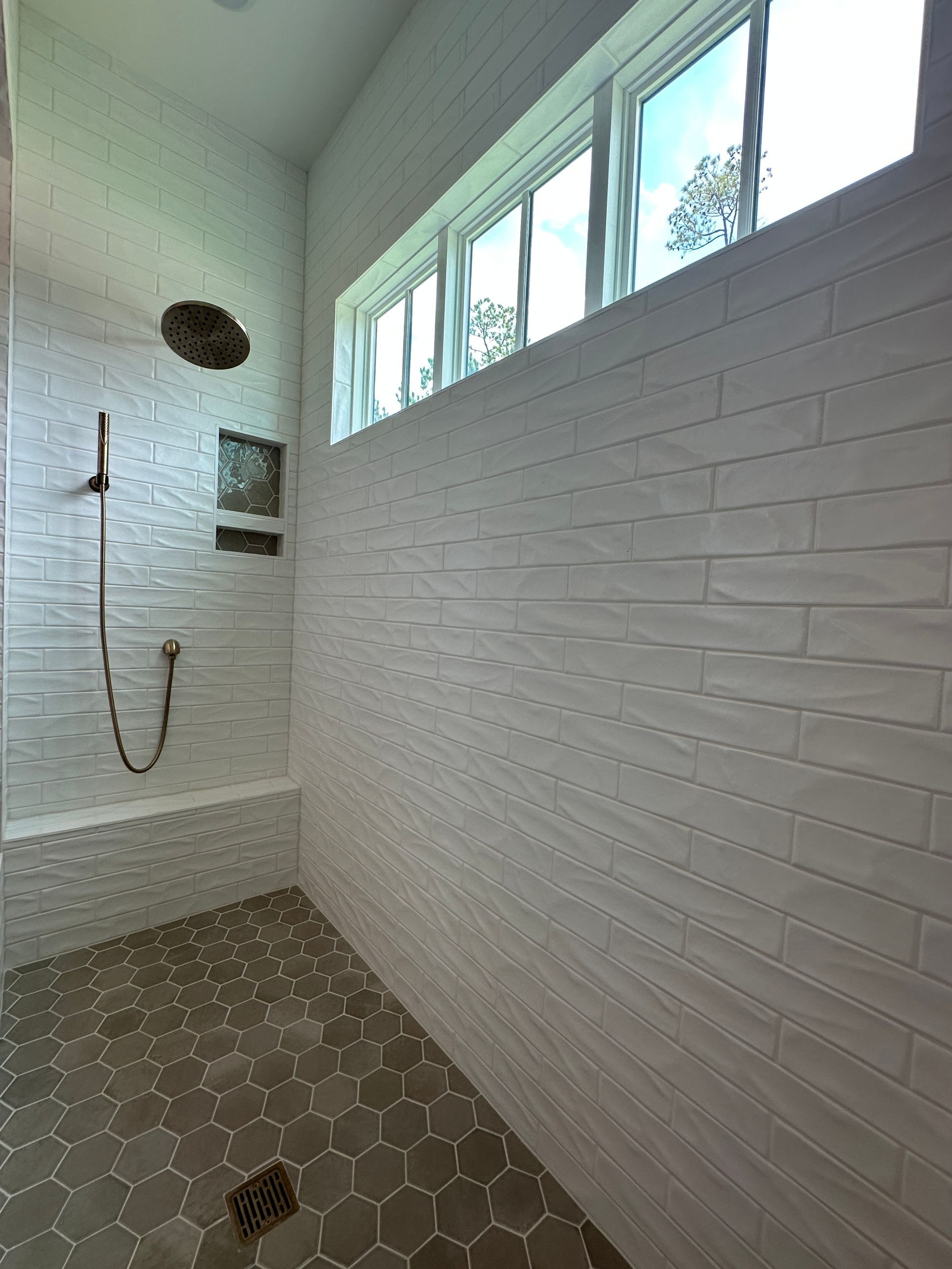Small tiled shower with white brick walls, hex floor tiles, and a high frosted window.