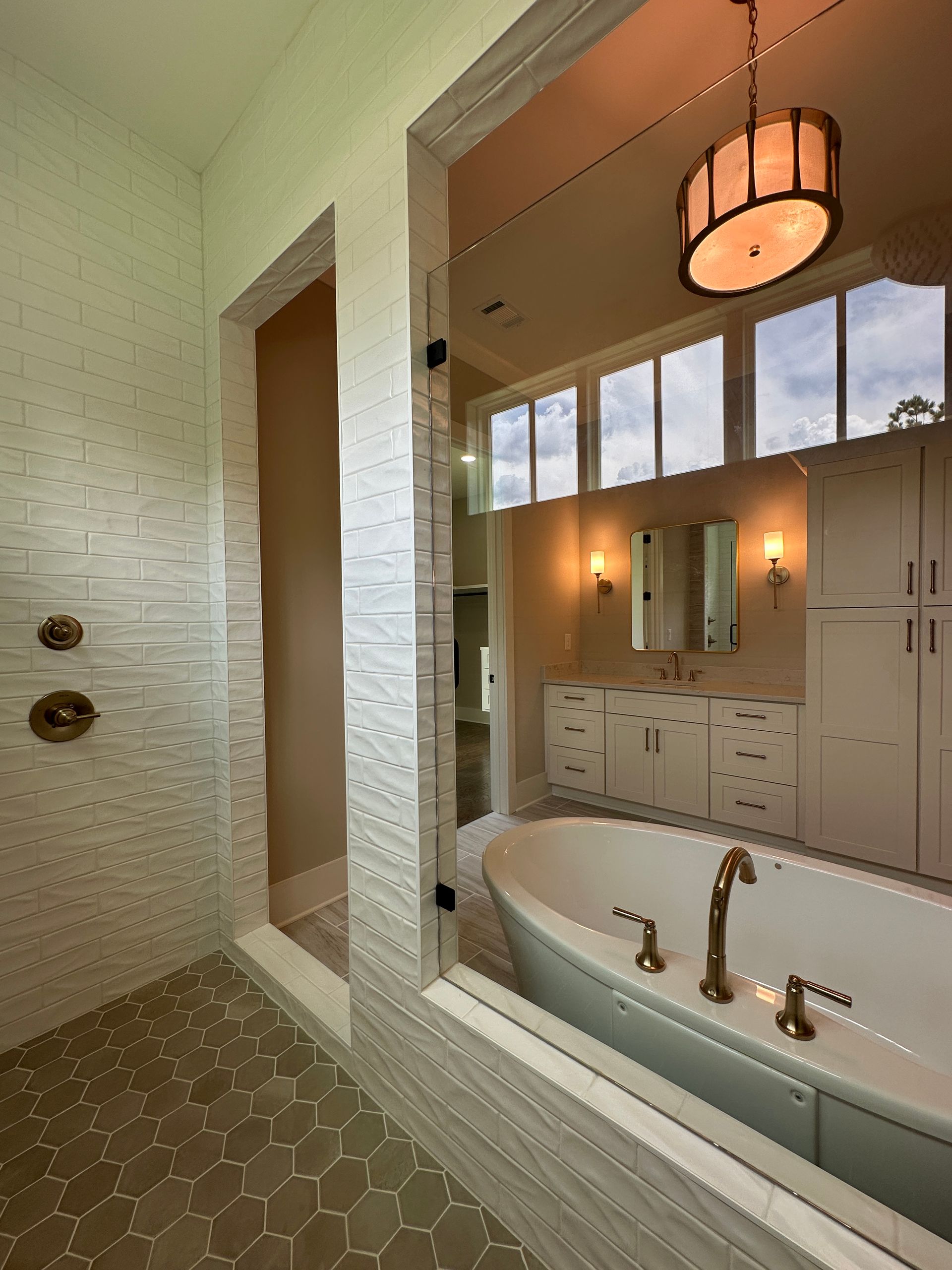 Bathroom view with green tiled shower, white tub, and warm pendant light reflecting in mirror