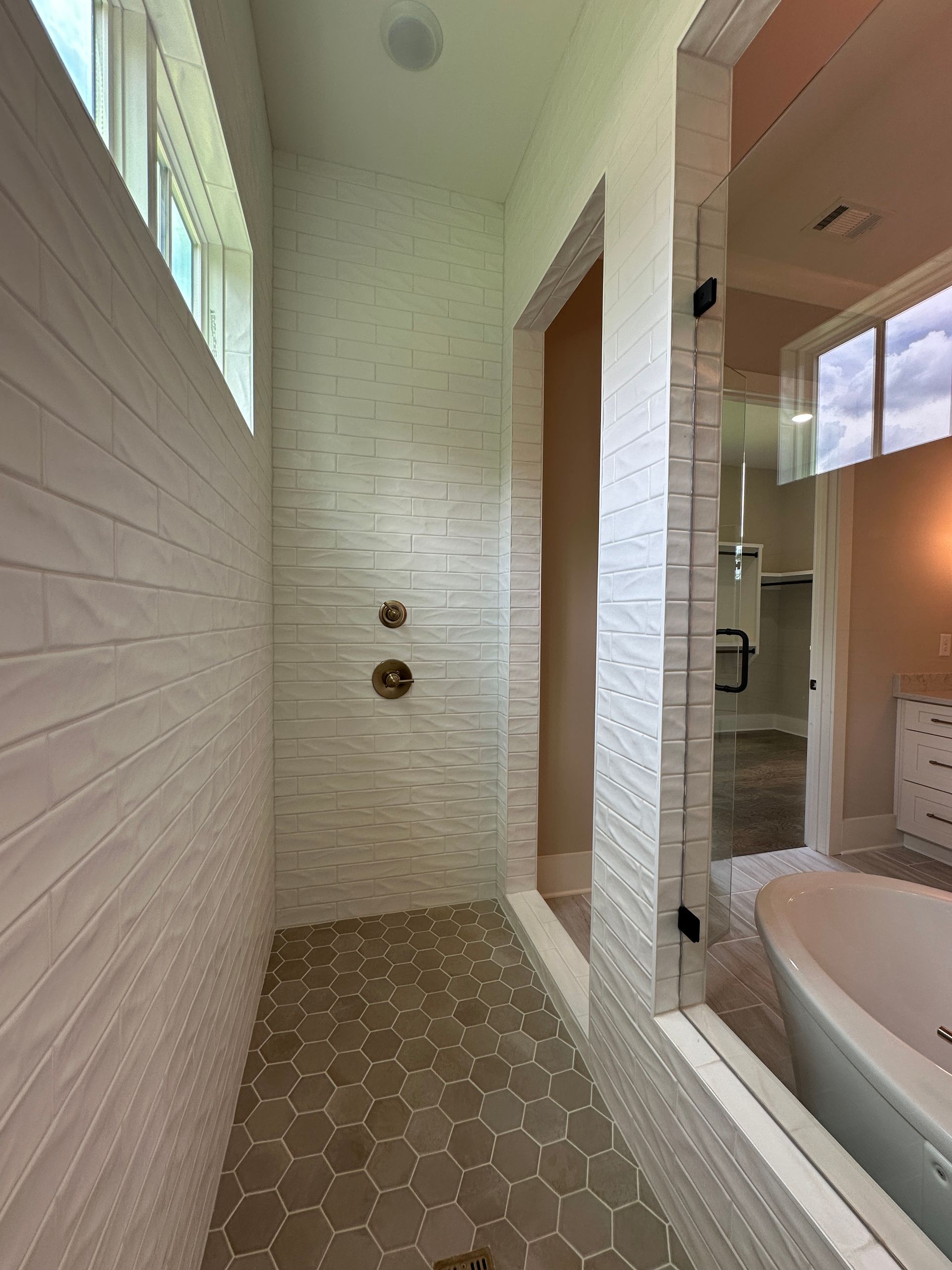 Bright white tiled shower and tub area with hexagon floor tiles and glass enclosure