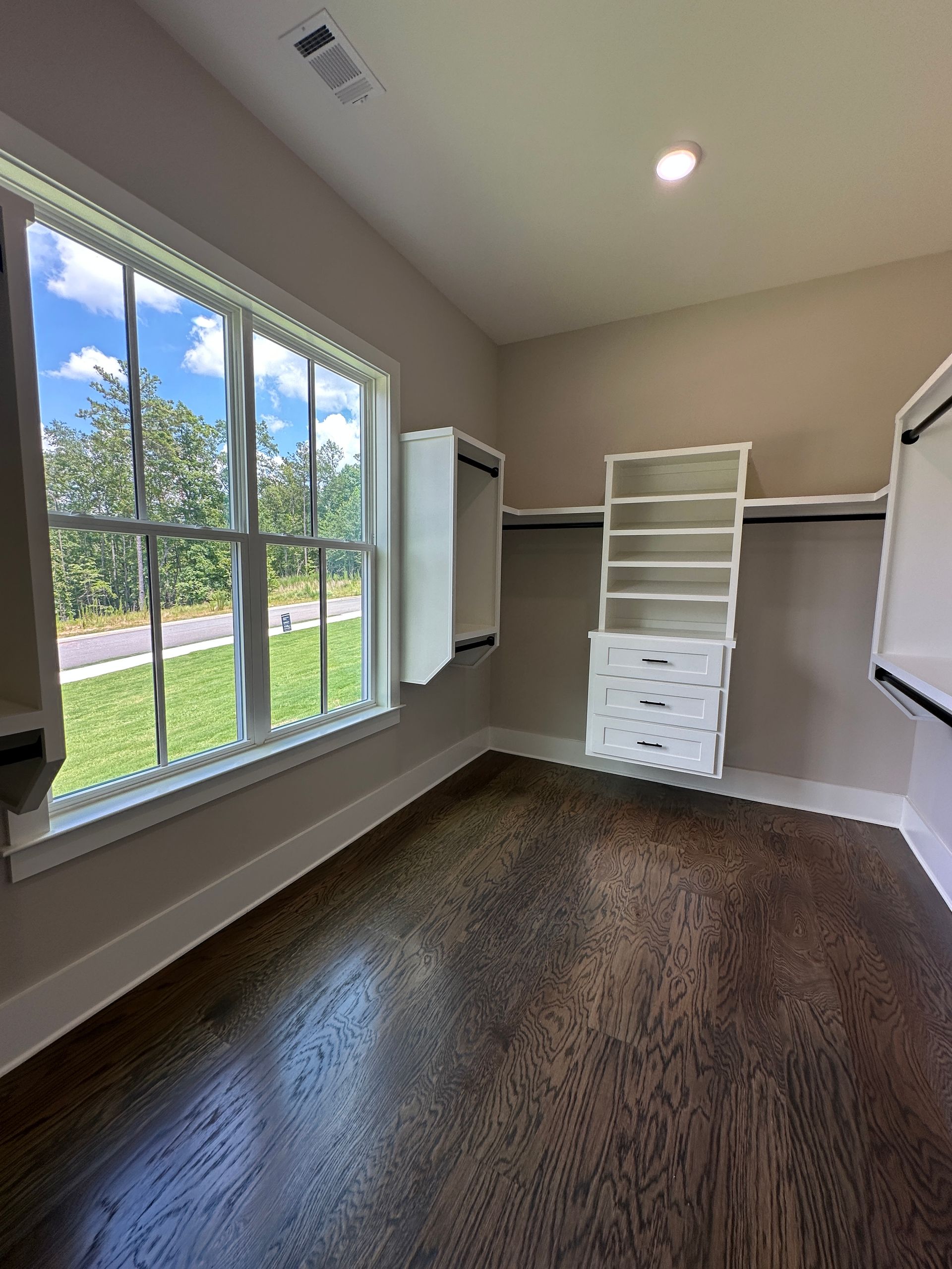 Empty walk-in closet with white shelving, brown wood floor, and a large window.