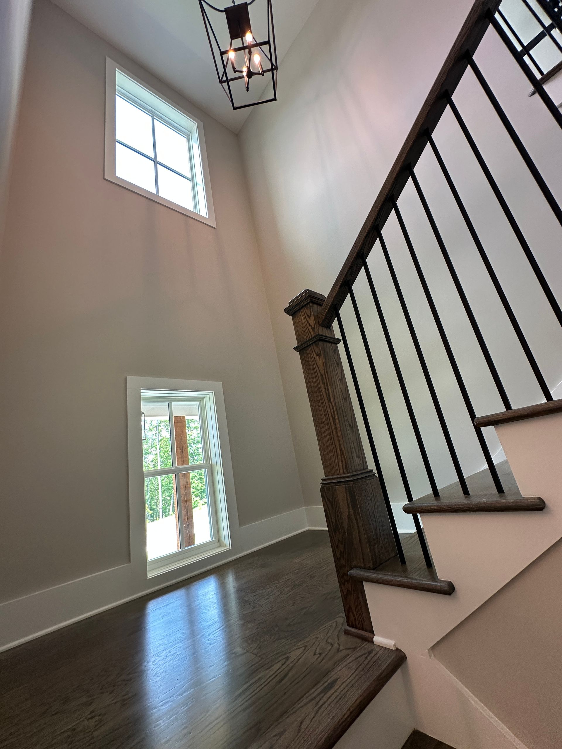 Staircase with dark iron railing, white walls, hardwood floor, and a window bringing in daylight.