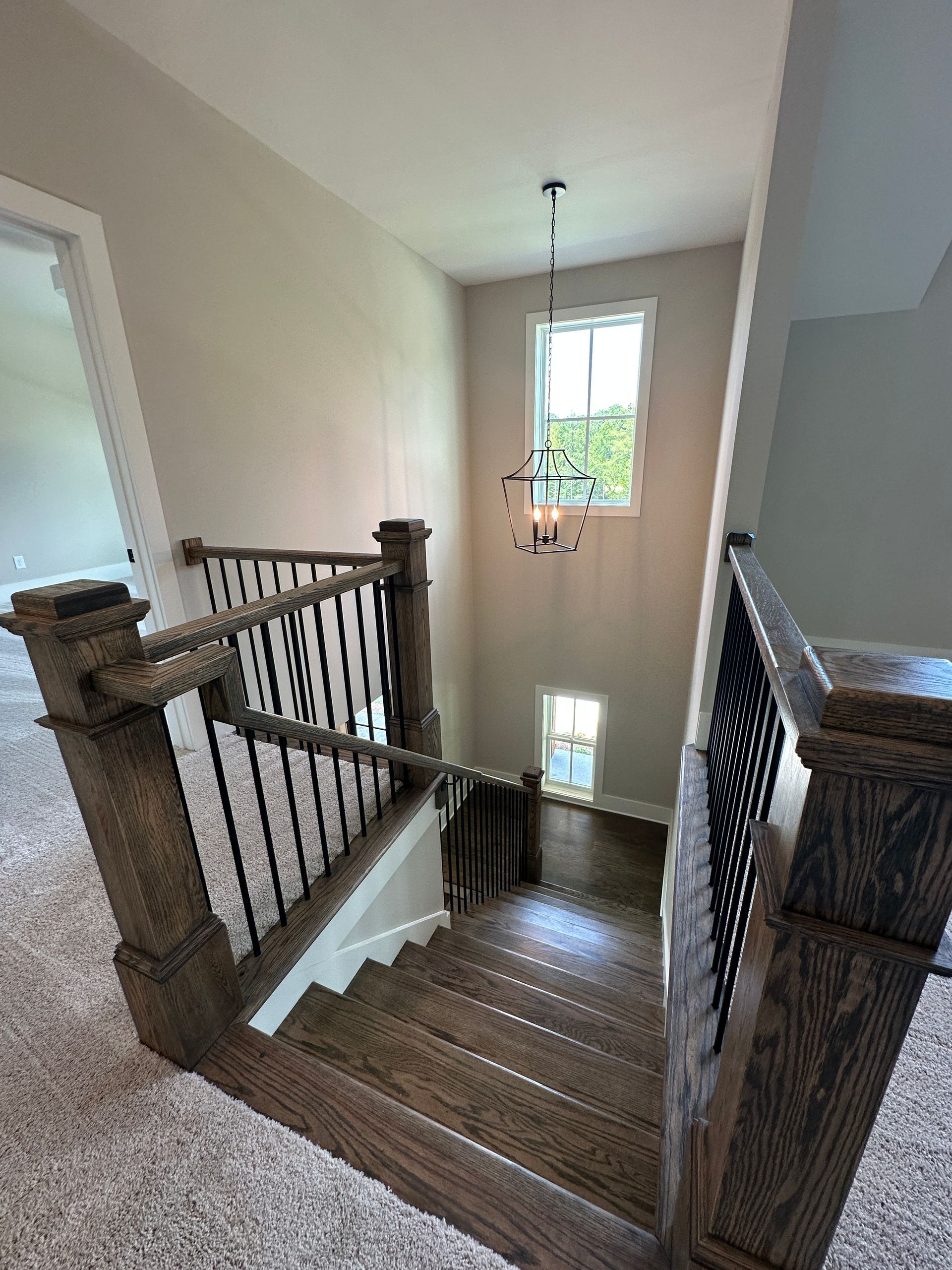 Stairwell landing with wooden banister, carpeted steps, and a window at the end of the hall.