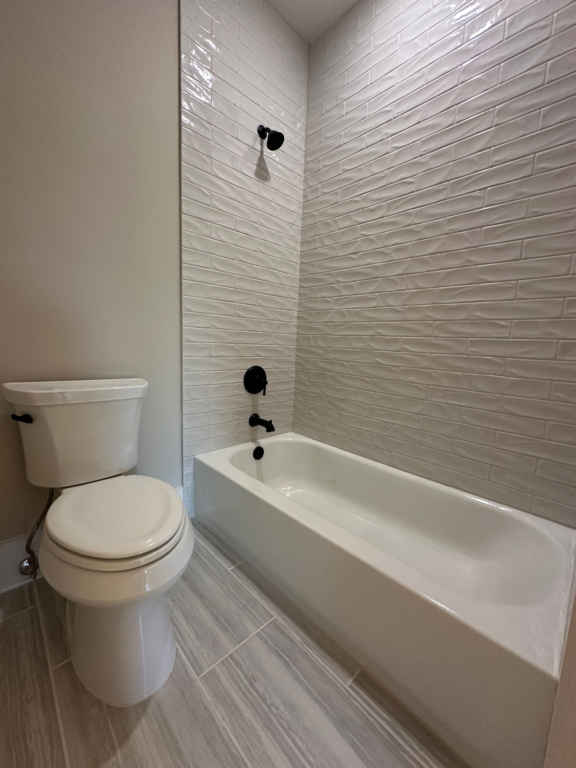 Small bathroom with toilet and white bathtub, light gray tile floor, and textured white shower wall.
