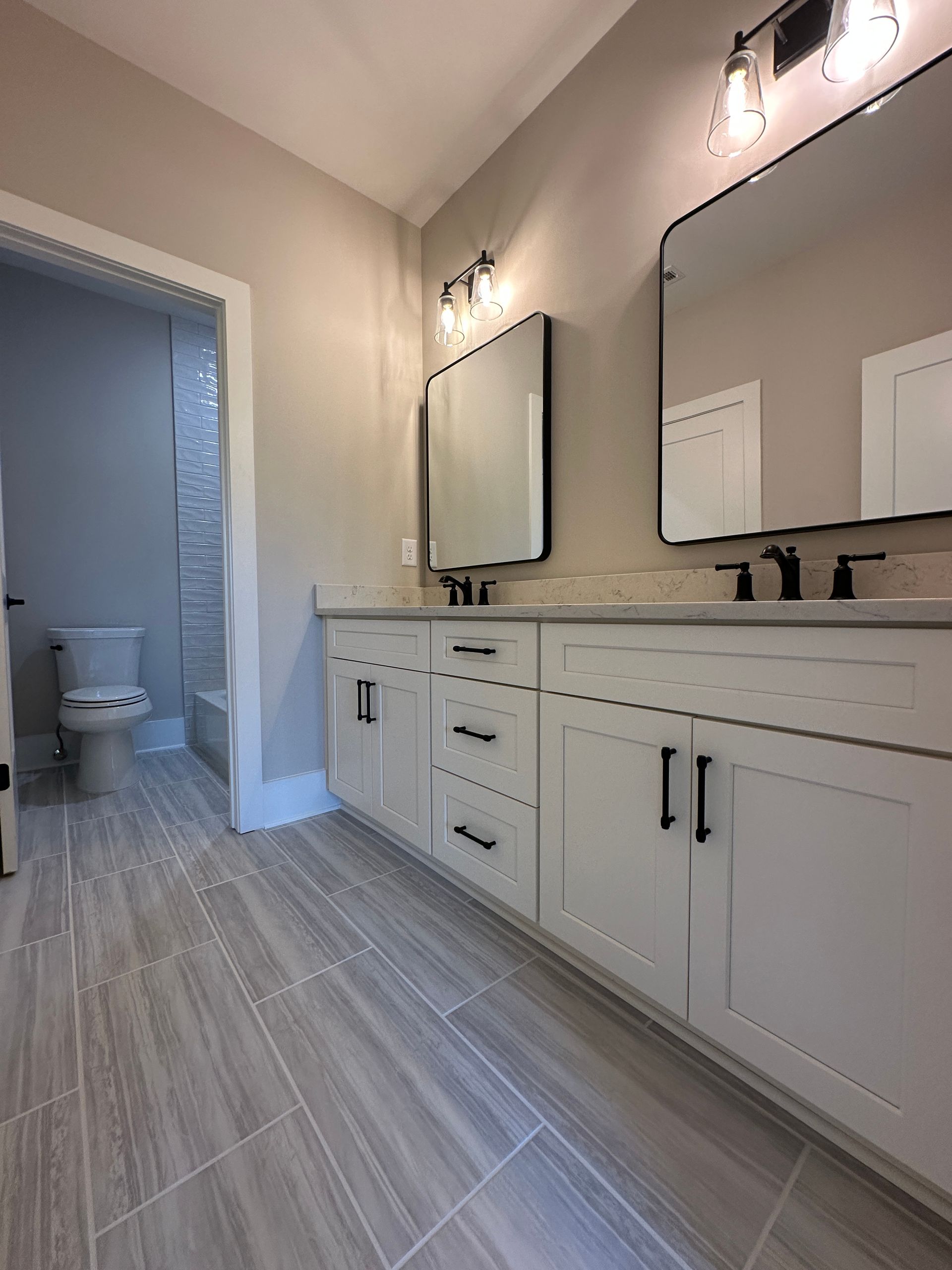Modern bathroom with double vanity, large mirrors, and an open toilet room in the background.