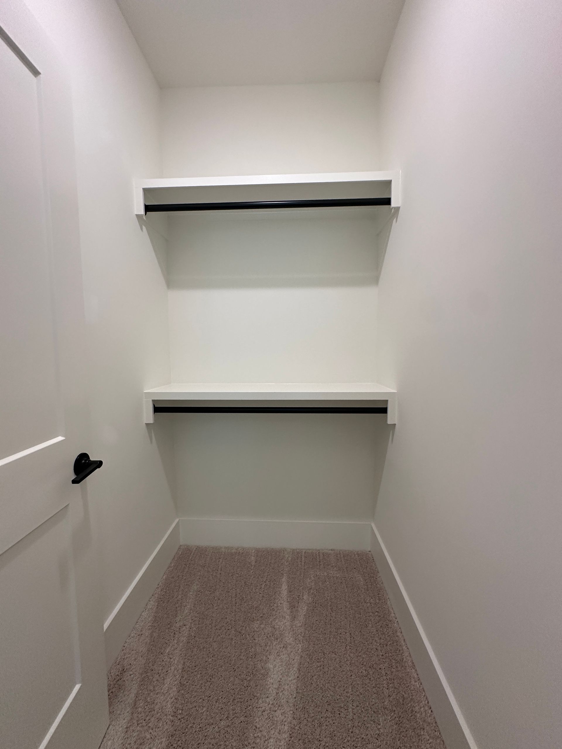 Empty white walk-in closet with two shelves and carpeted floor