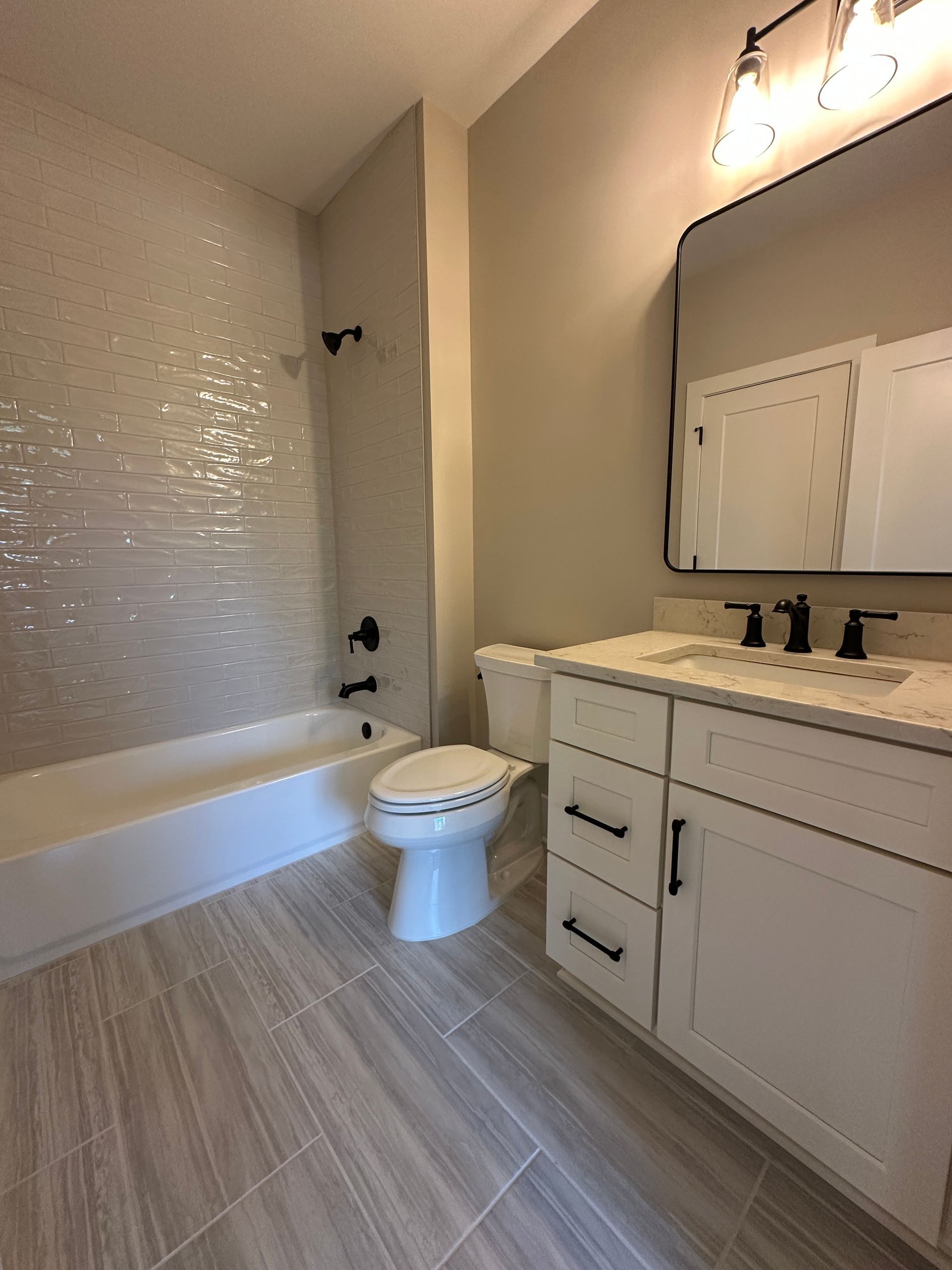 Modern bathroom with white vanity, toilet, bathtub, and tiled shower wall