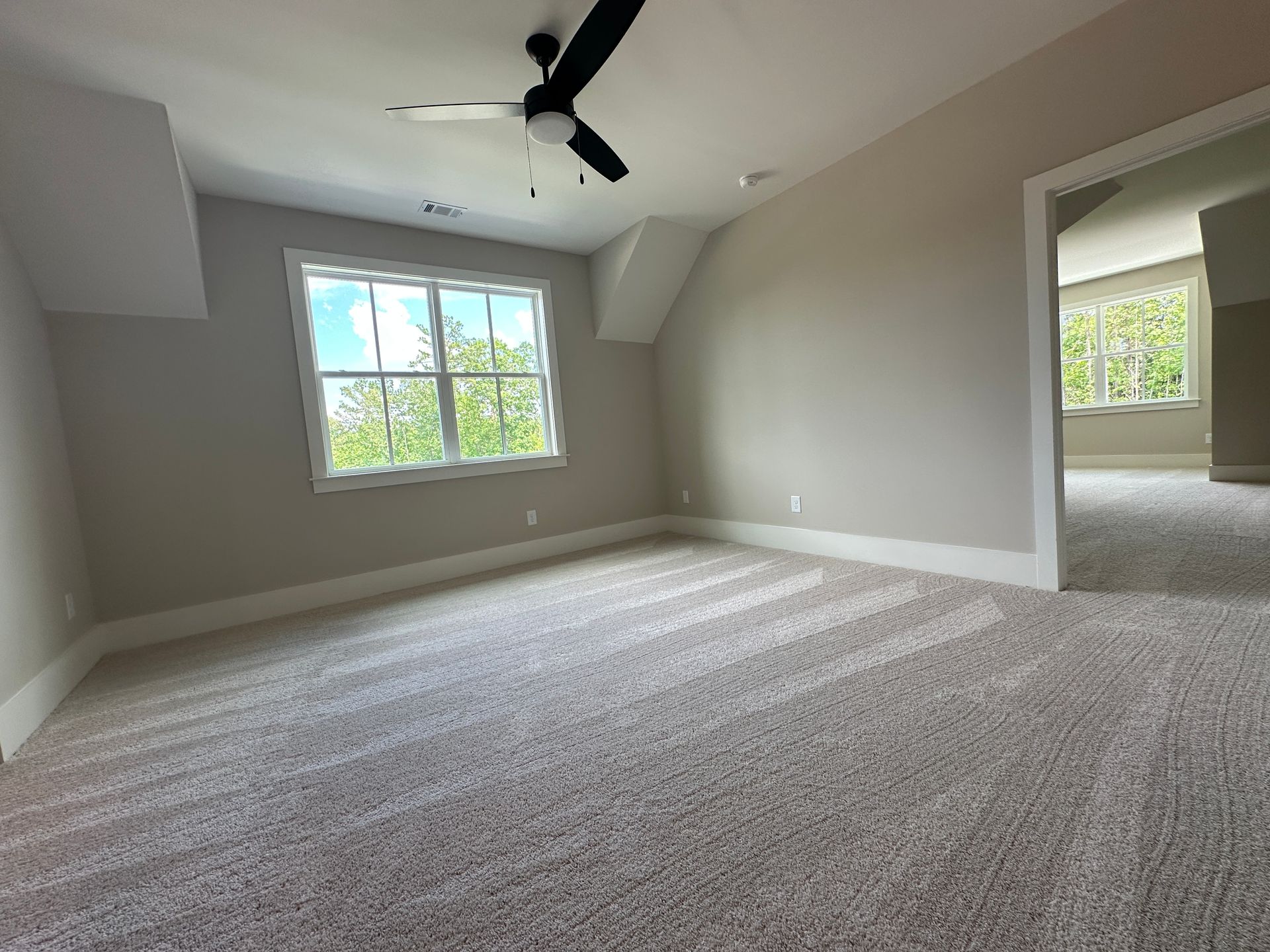 Empty carpeted bedroom with gray walls, white trim, ceiling fan, and a window letting in daylight
