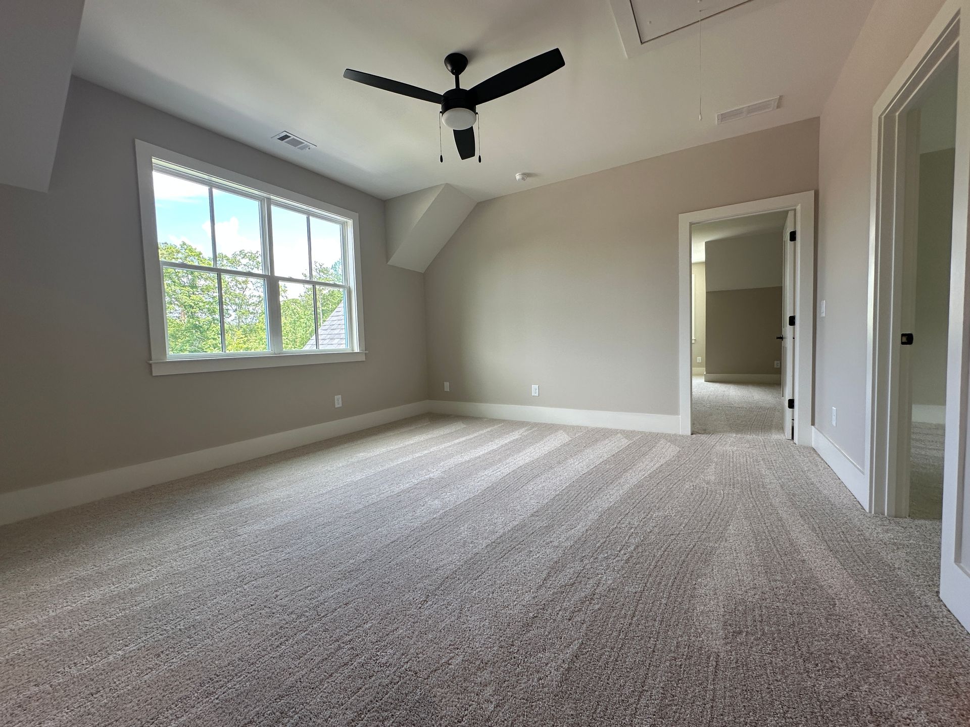 Empty carpeted bedroom with gray walls, window light, ceiling fan, and open doorway