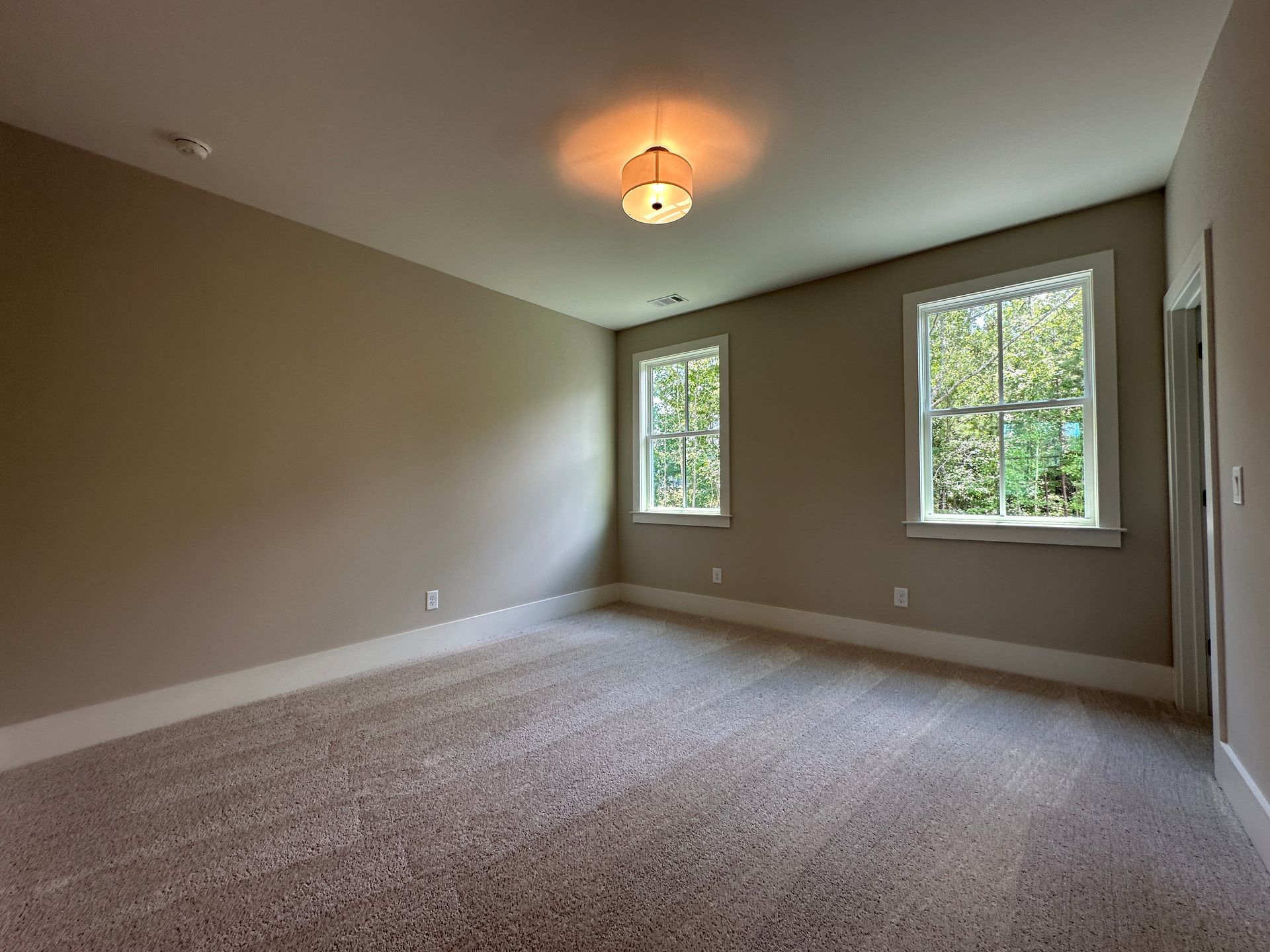 Empty beige carpeted bedroom with two windows and a ceiling light