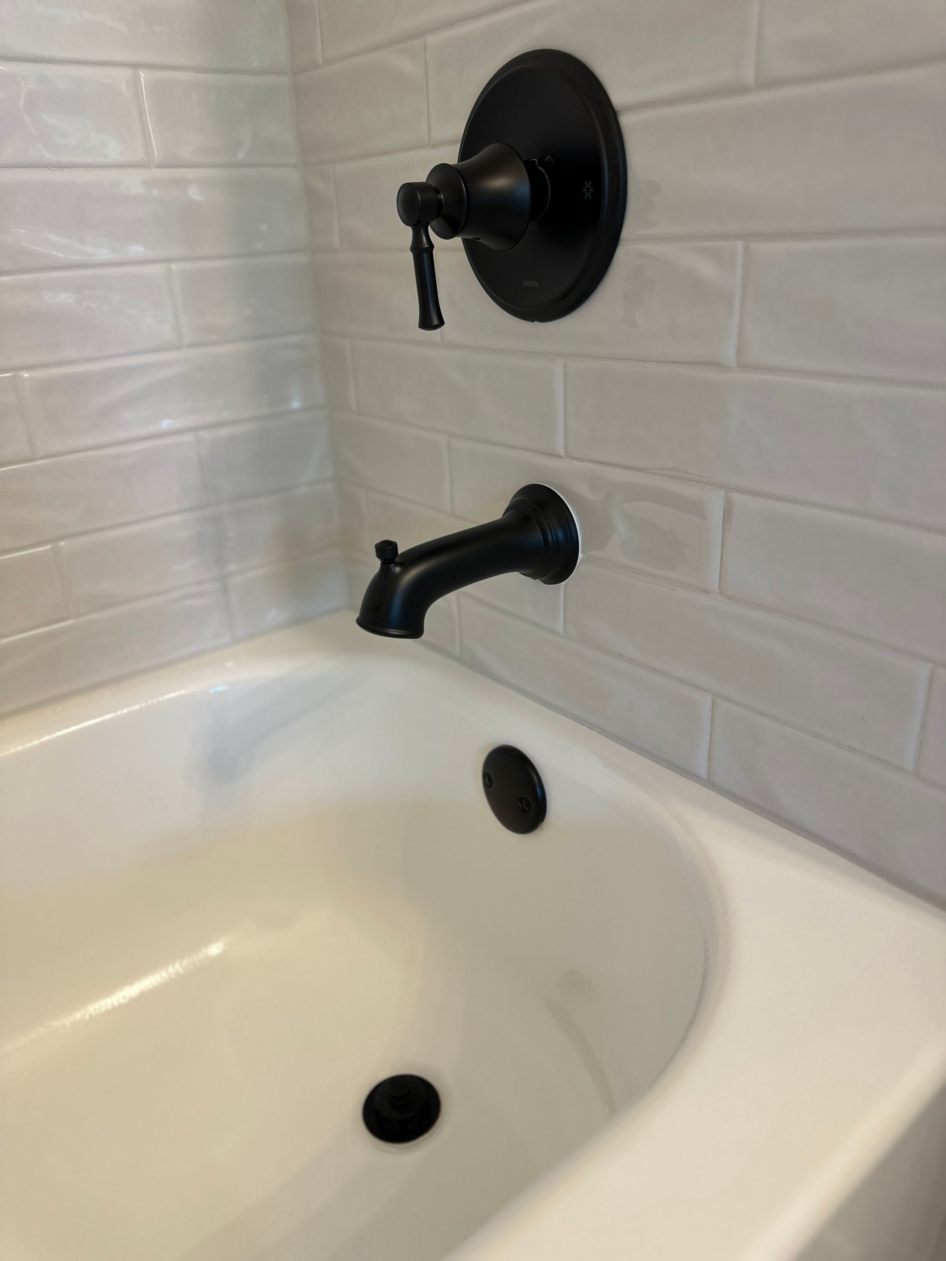 White bathtub with black faucet, shower control, and tiled wall corner