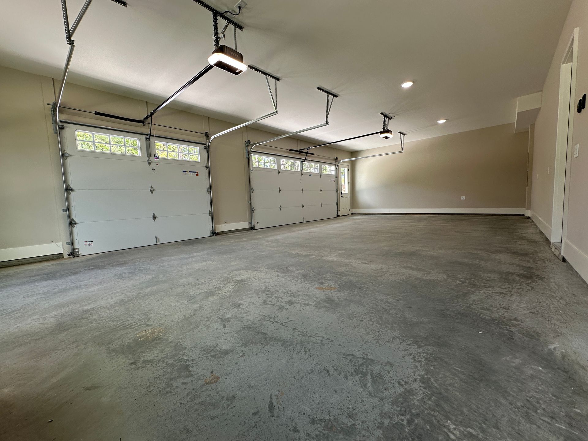 Empty two-car garage with gray concrete floor, beige walls, and three white garage doors.
