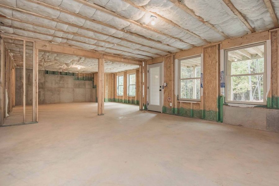 Unfinished basement interior with exposed wooden beams, concrete floor, windows, and door.