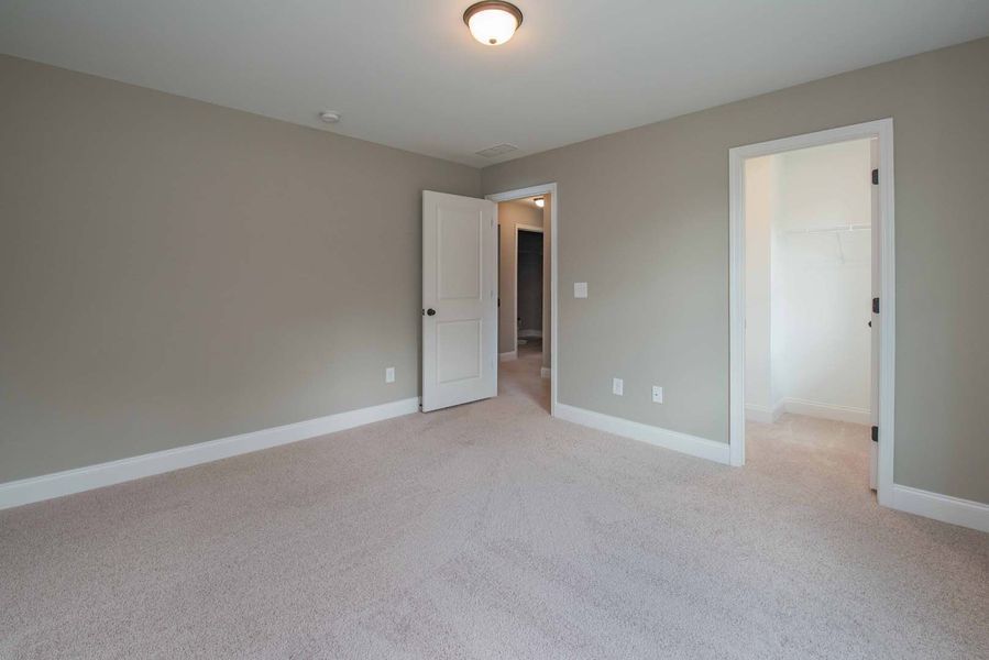 Empty bedroom with gray walls, white trim, and beige carpet. Two doorways lead to other rooms.