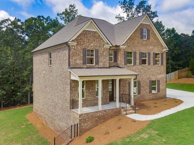 Two-story brick house with brown shutters, porch, and driveway on a grassy lot.