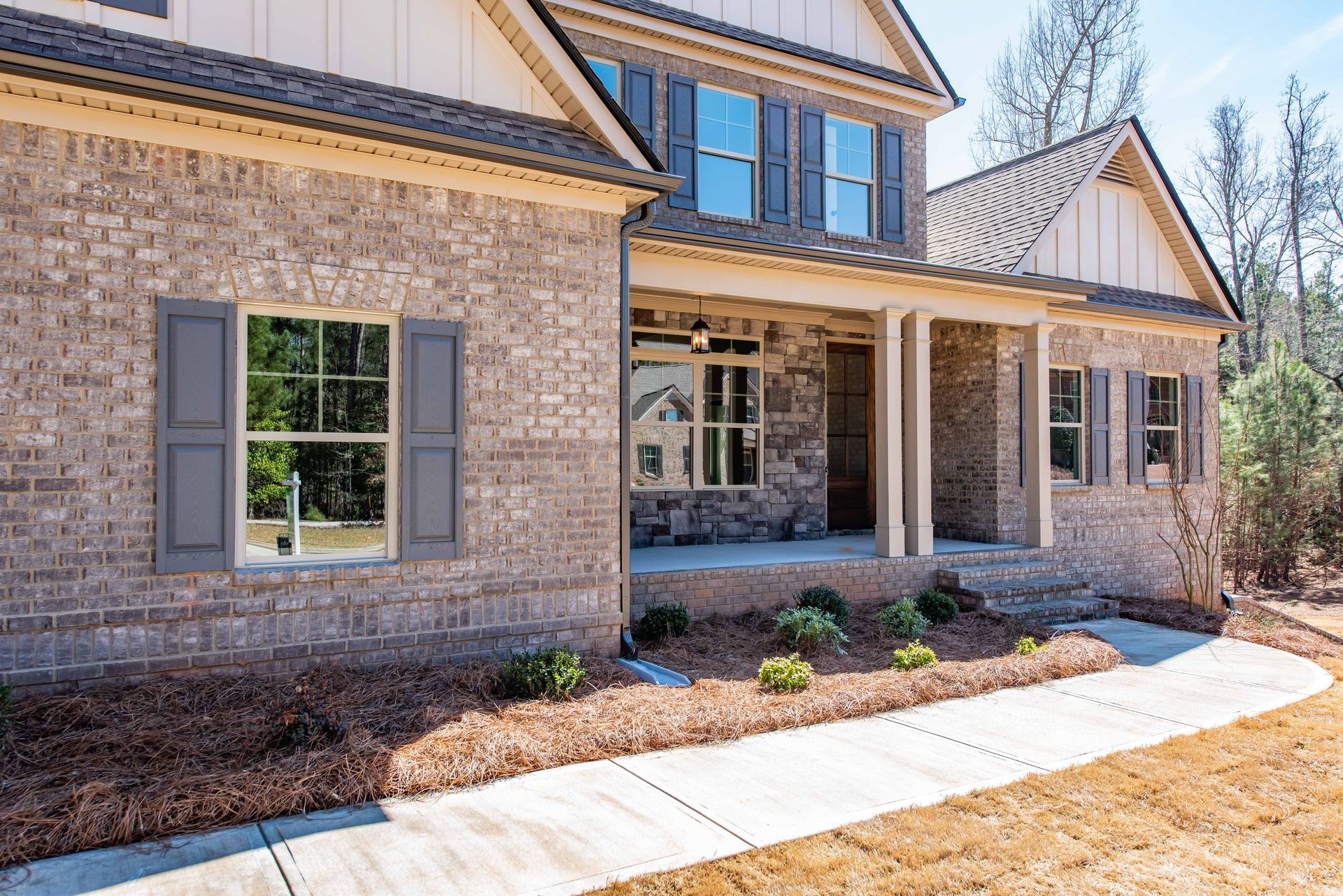 Brick suburban house with covered porch, gray shutters, and white walkway in front yard
