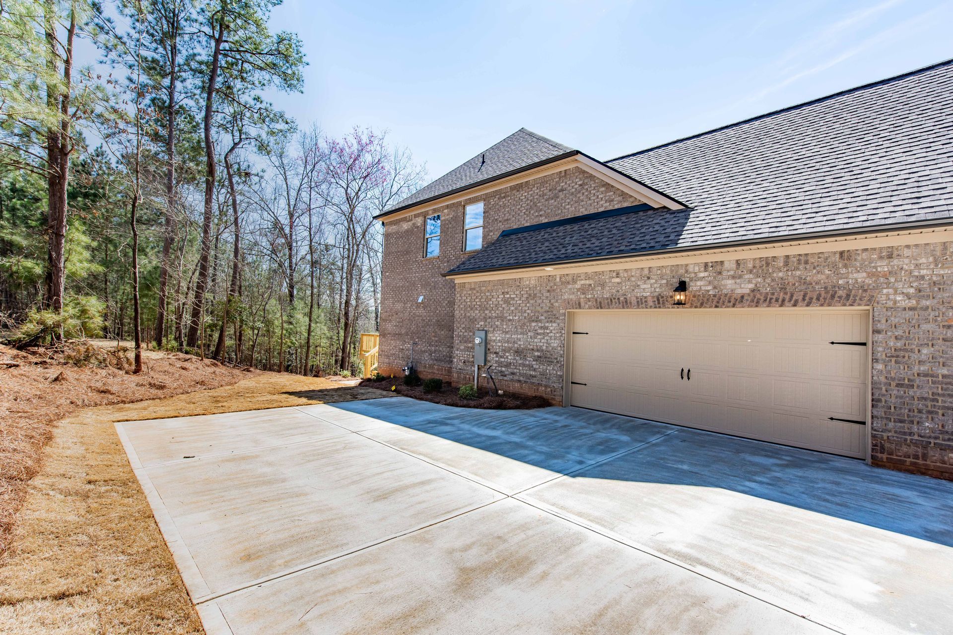 Stone house with a two-car garage and wide concrete driveway beside a wooded lot