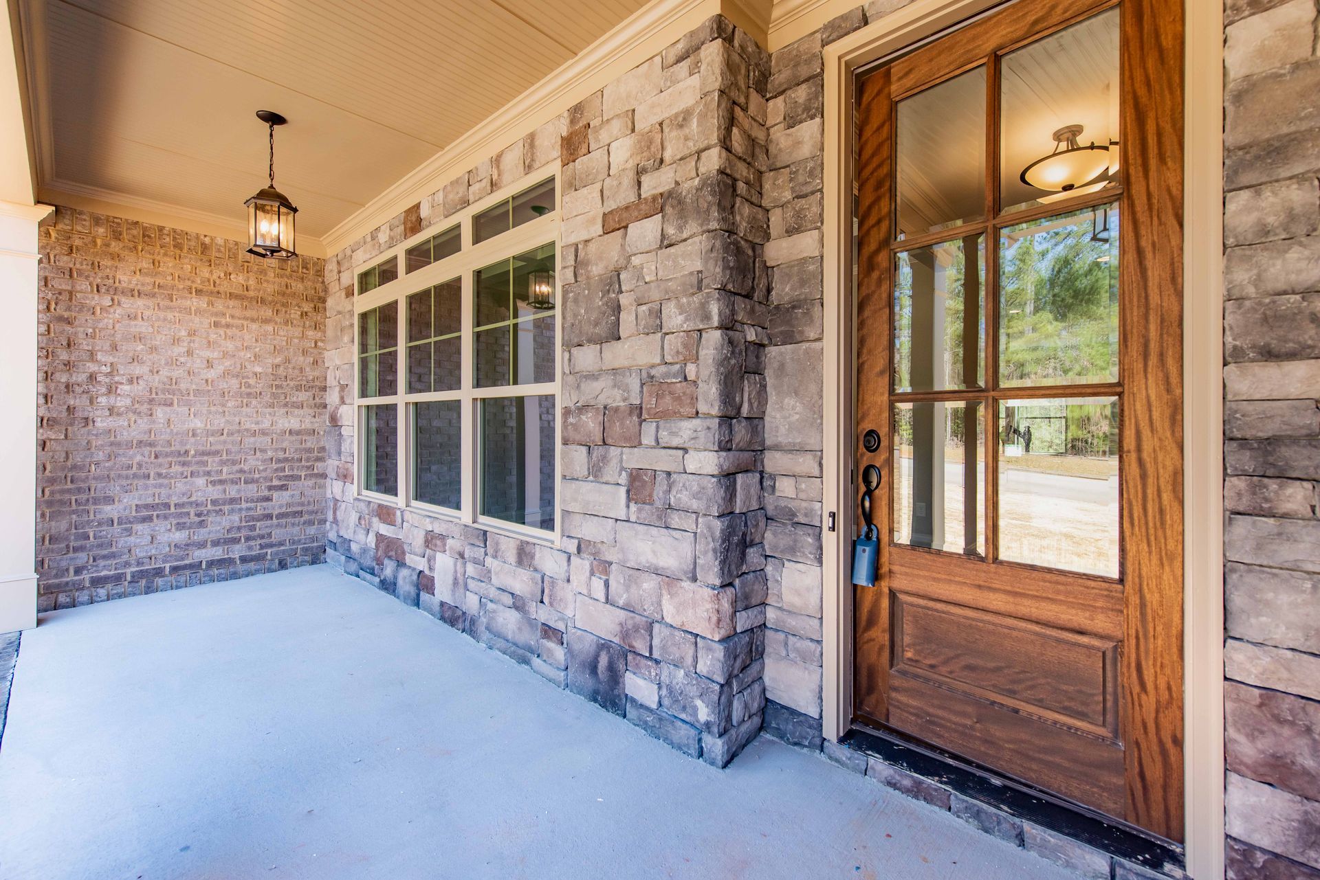 Covered front porch with stone walls, large windows, and a wooden door with glass panels.