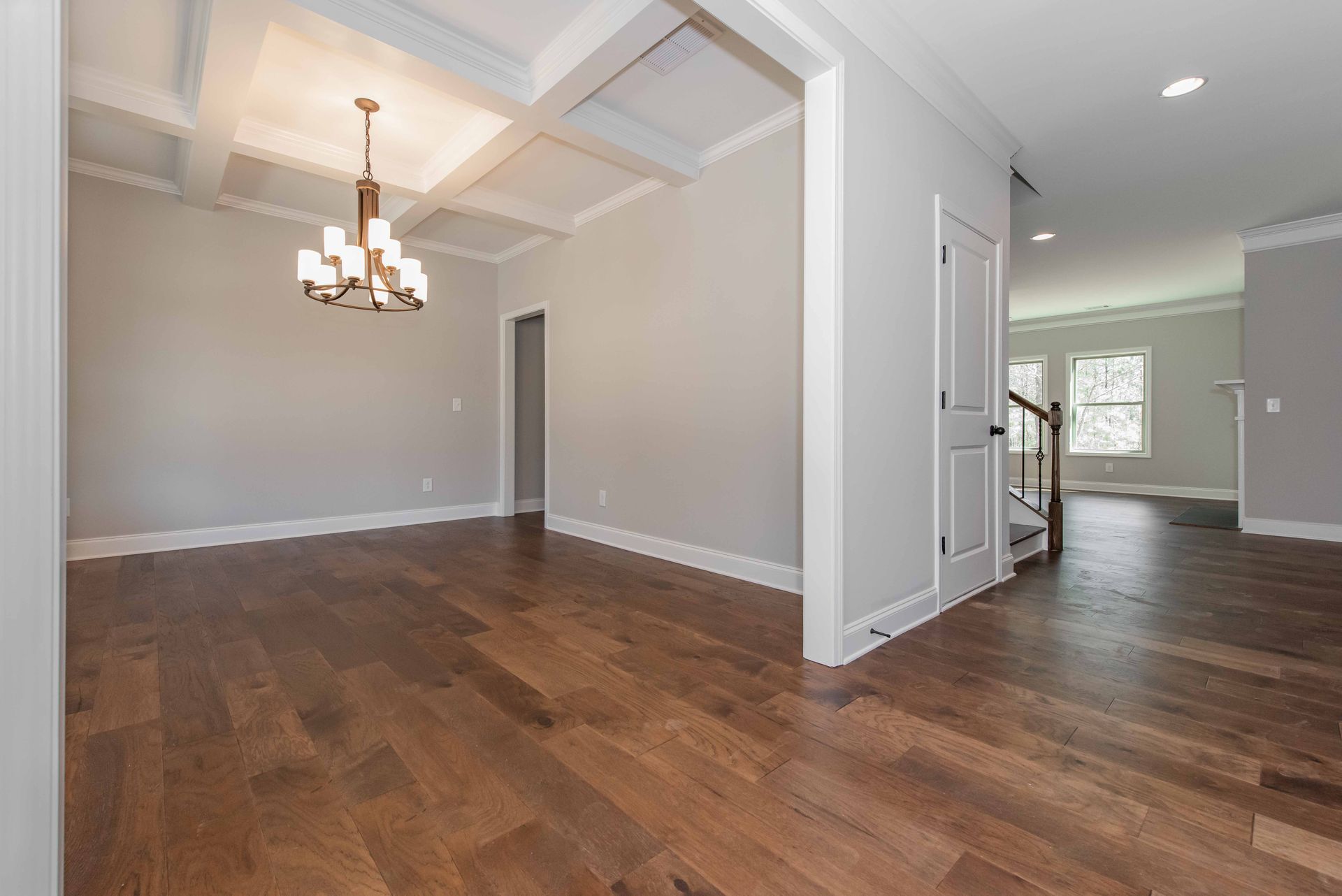 Empty open-plan dining and living room with hardwood floors, gray walls, and a chandelier.