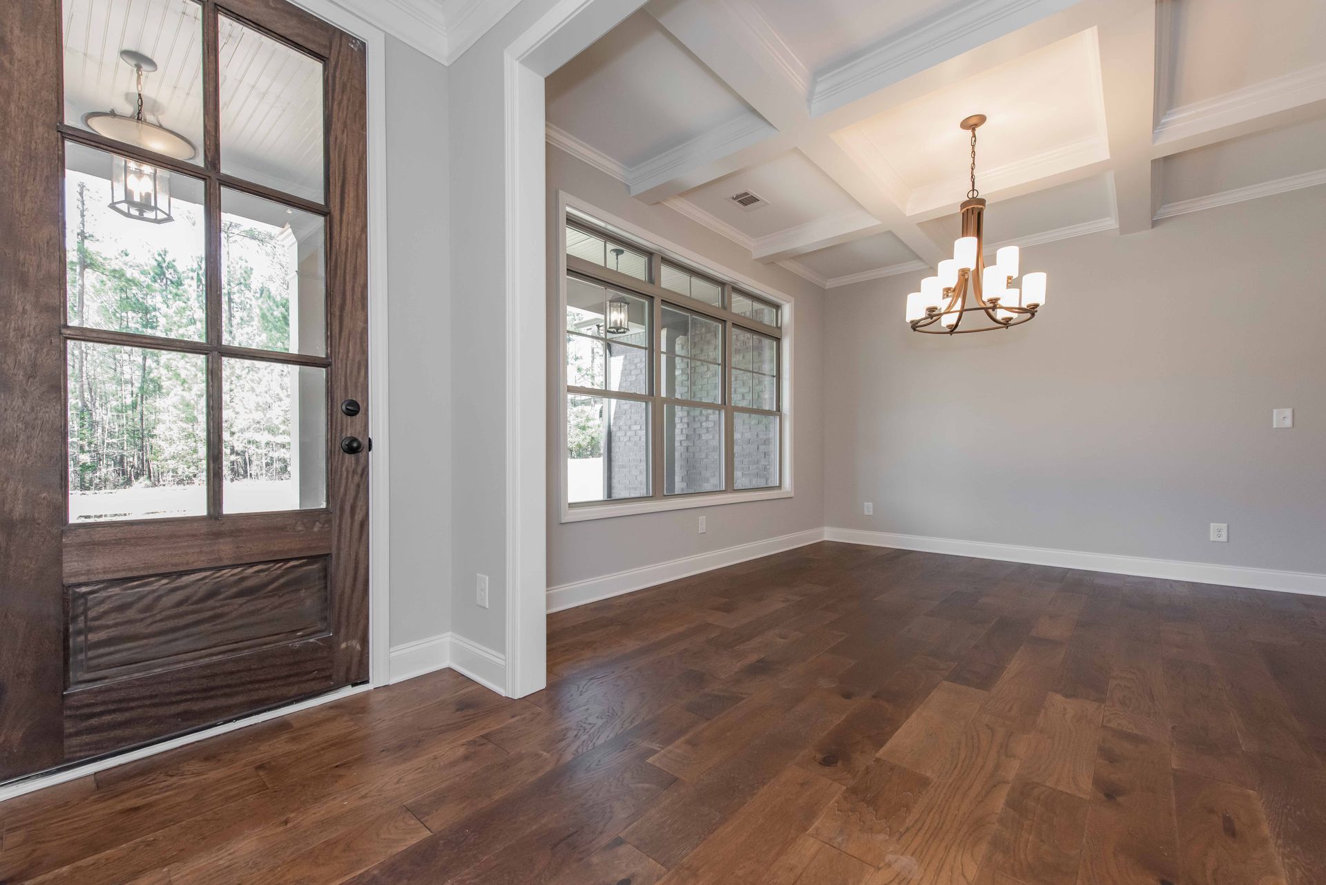 Empty dining room with hardwood floors, gray walls, wood front door, and chandelier.