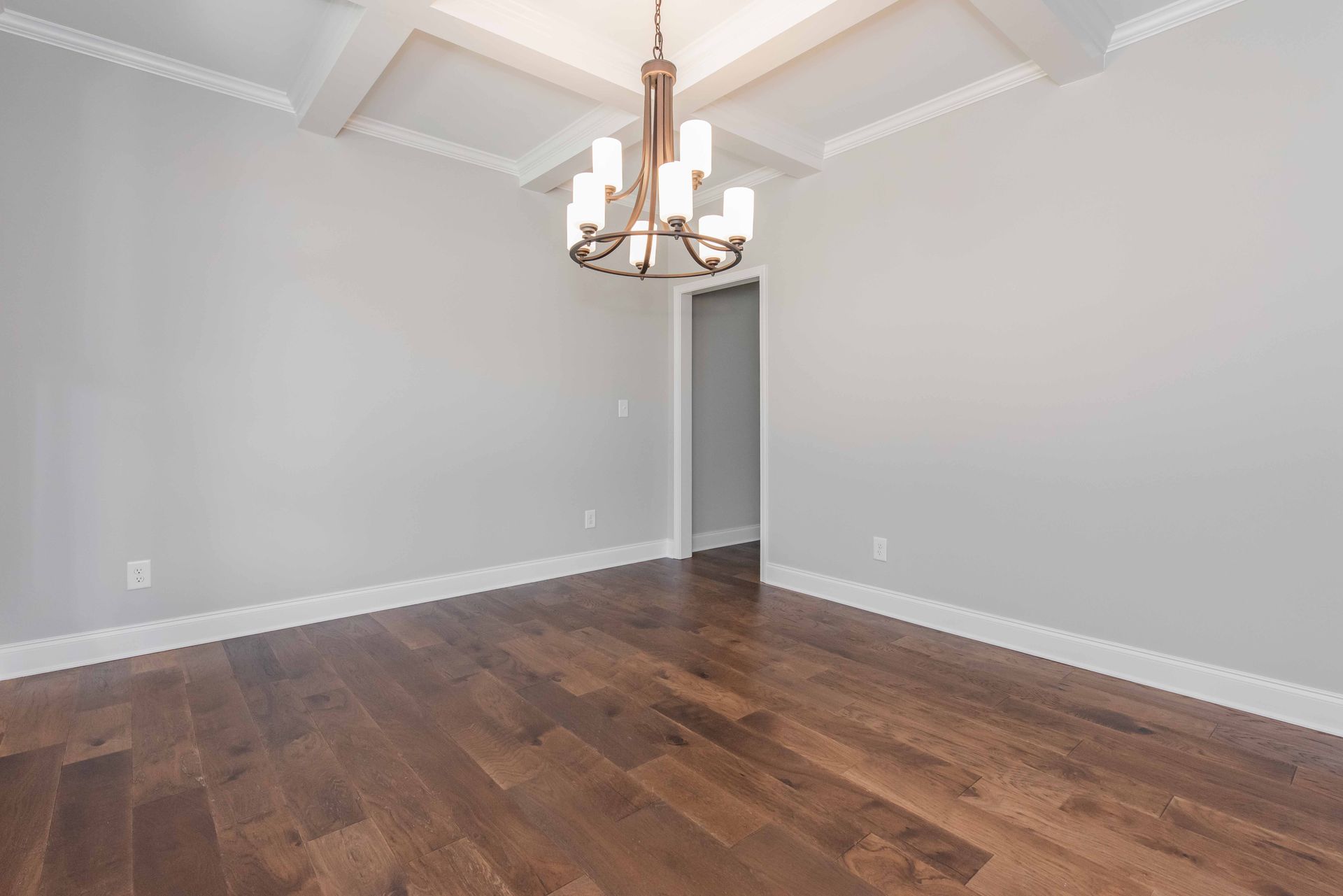 Empty dining room with dark wood floor, light gray walls, and a chandelier on a coffered ceiling.