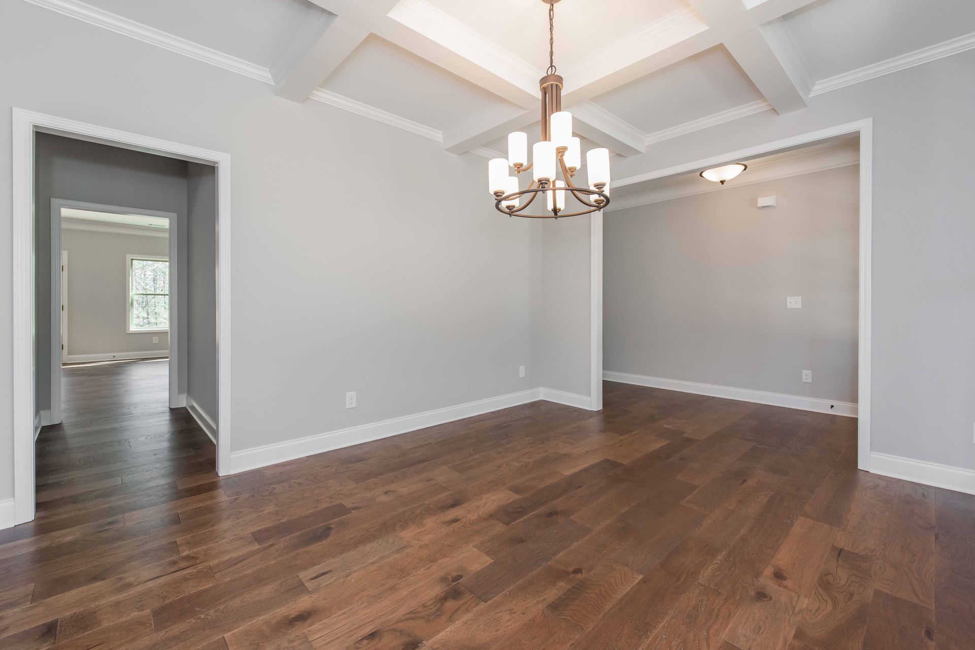 Empty dining room with gray walls, hardwood floors, and a chandelier