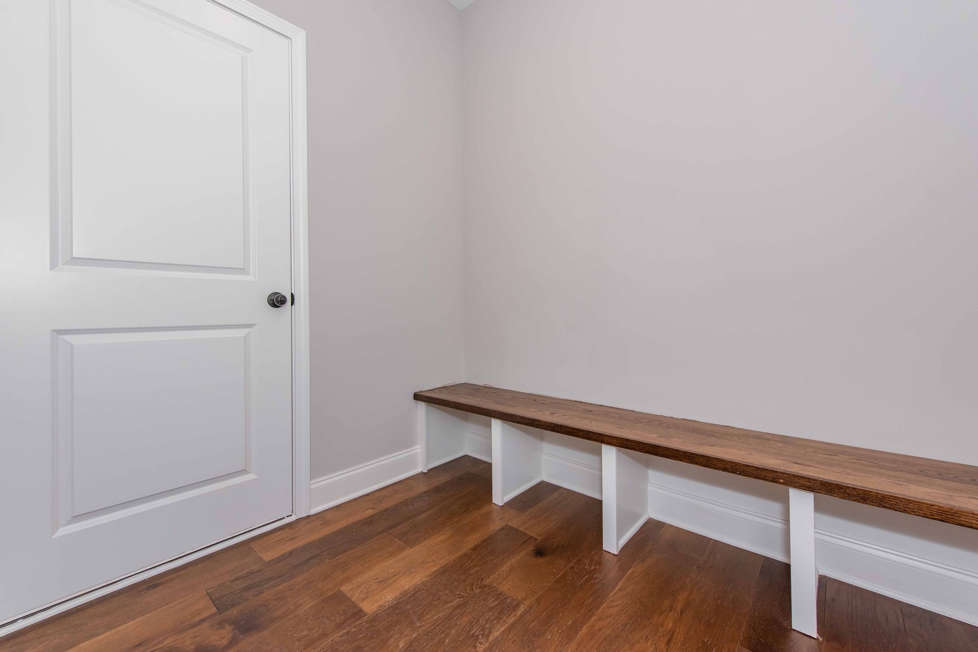 Empty room with white door, light gray walls, and a wooden bench along the wall.