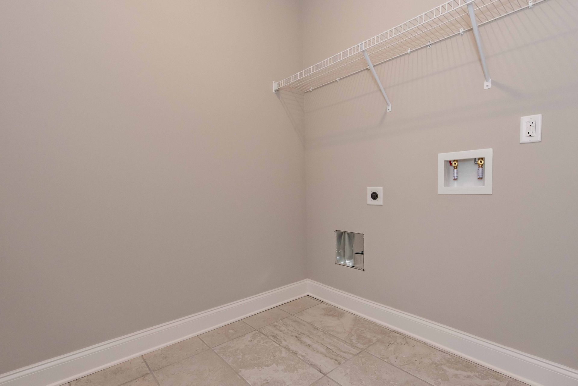 Empty laundry room with beige walls, tiled floor, wire shelf, and washer/dryer hookups on the right wall