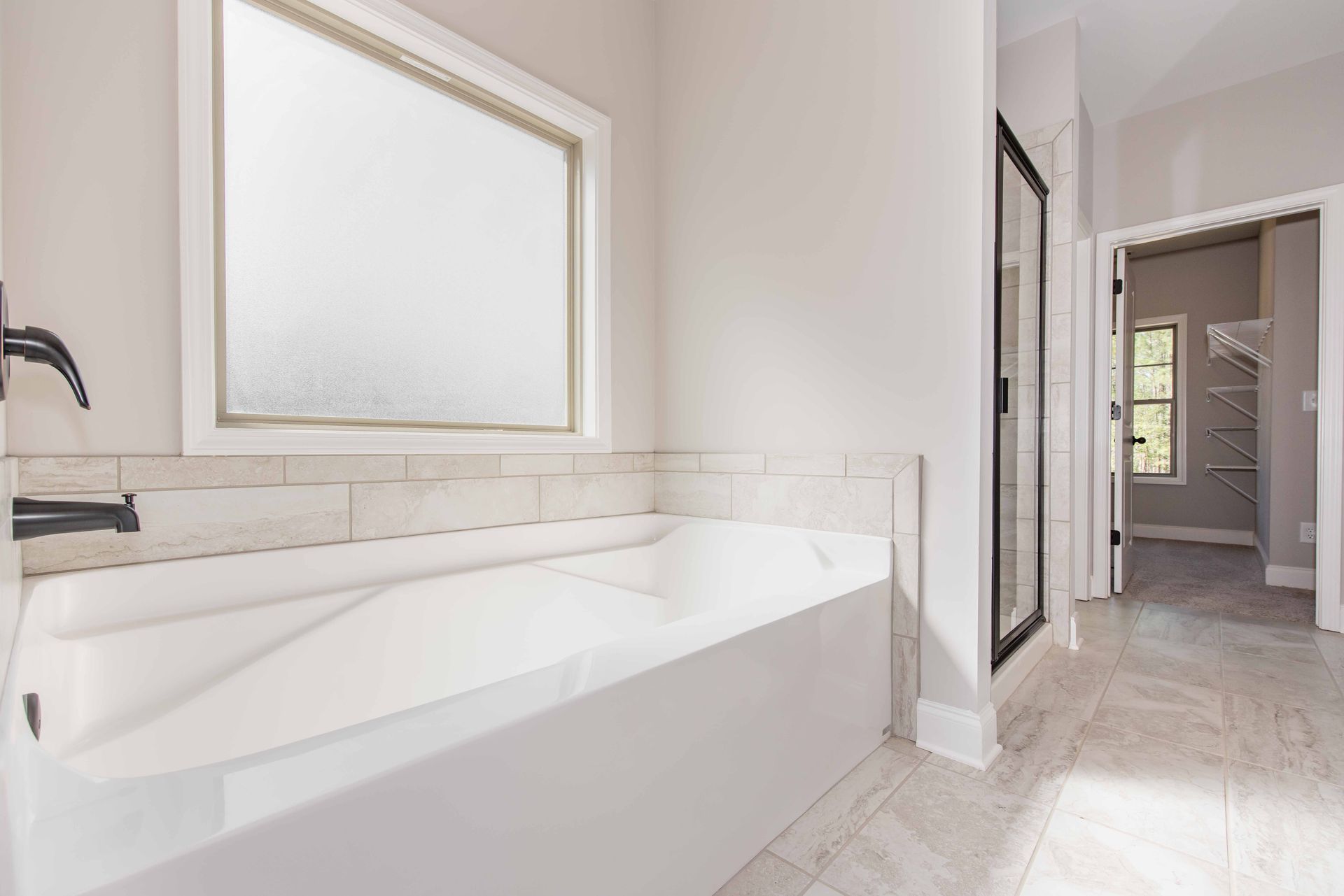 Bright bathroom with a white soaking tub, large mirror, and tiled floor leading to a hallway