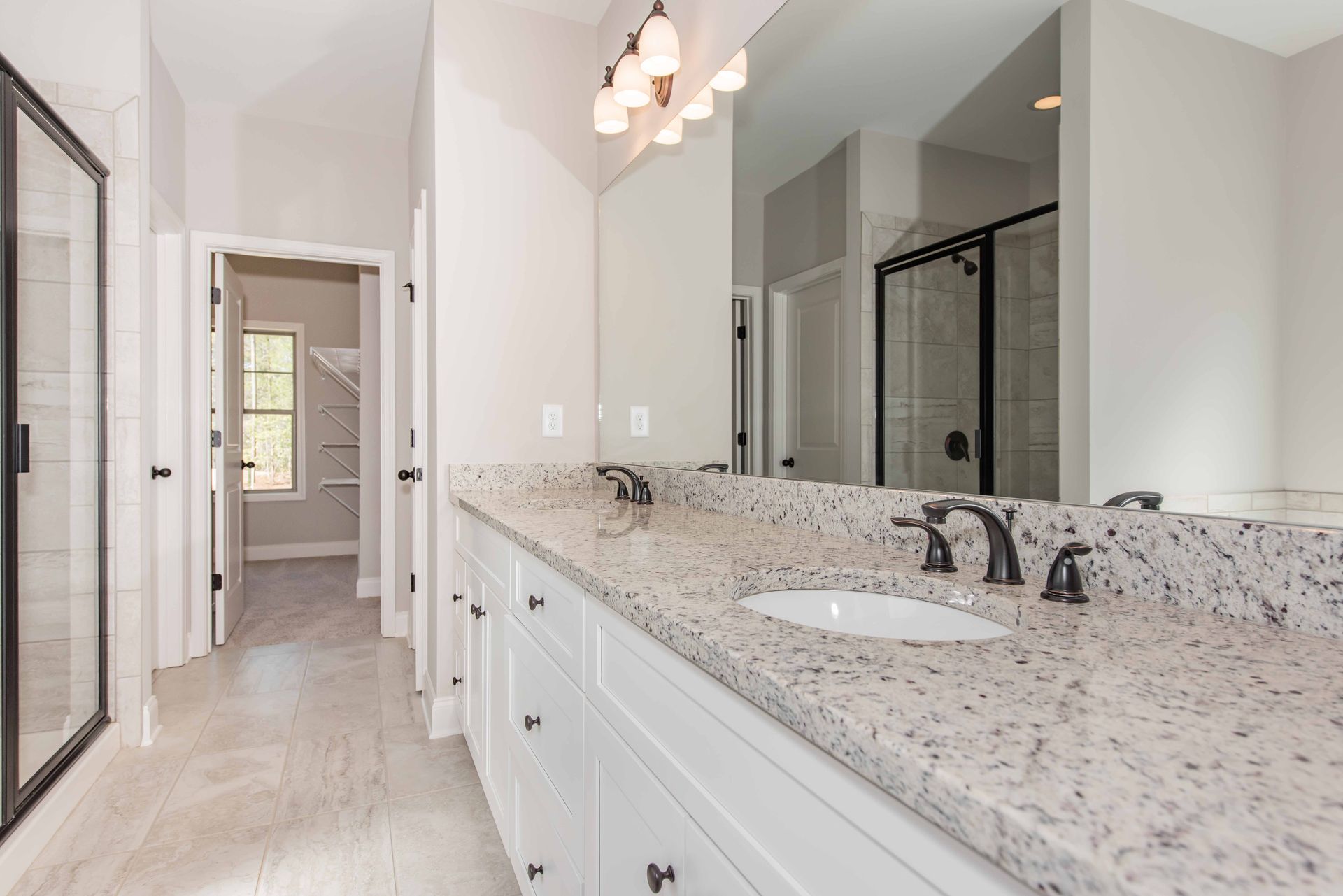 Bright bathroom vanity with granite countertop, double sinks, large mirror, and glass shower enclosure