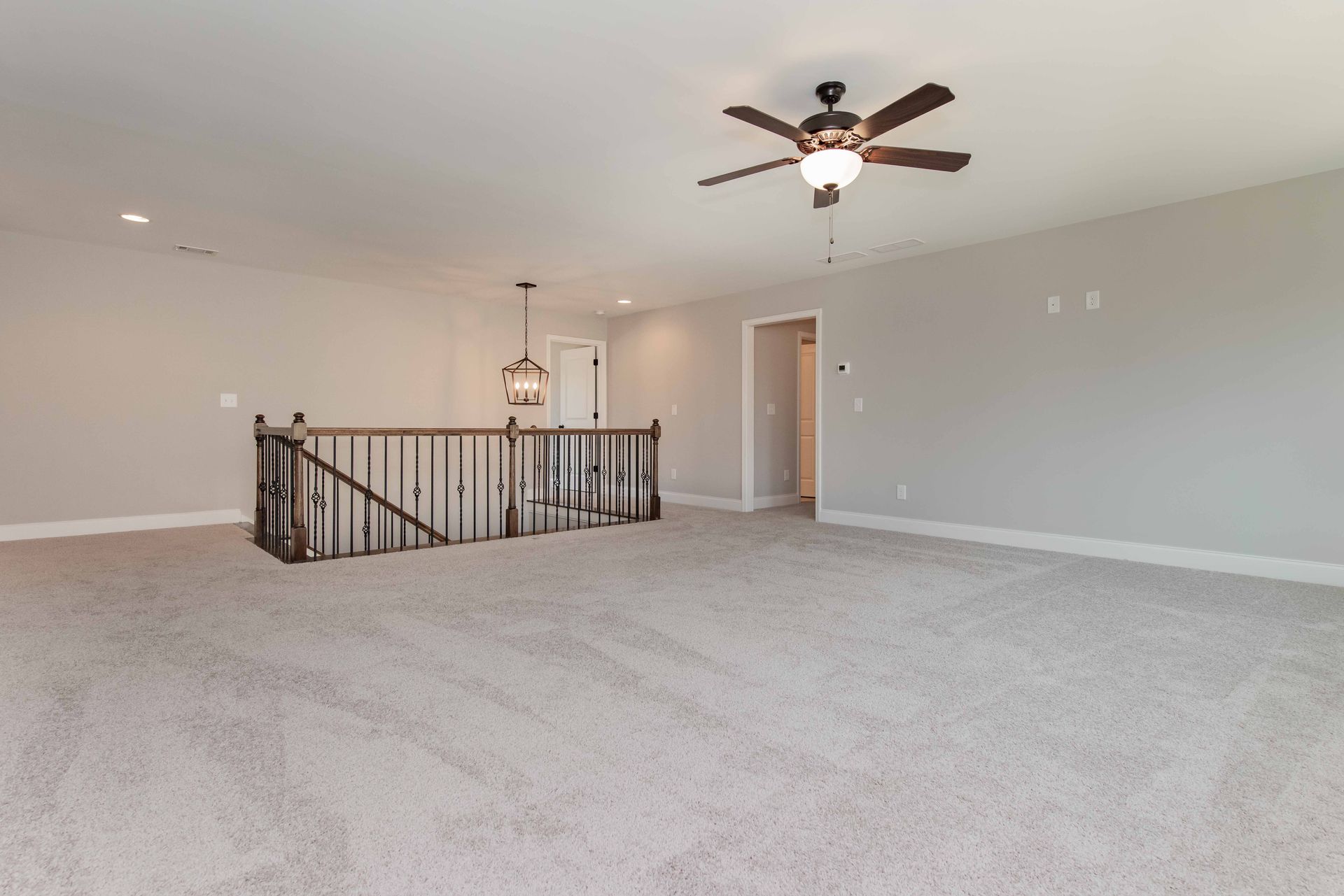 Spacious empty living room with carpet, ceiling fan, and staircase railing opening to a hallway