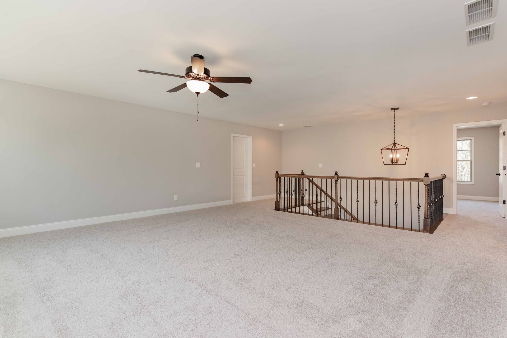 Spacious carpeted living room with ceiling fan, staircase railing, and chandelier by entryway
